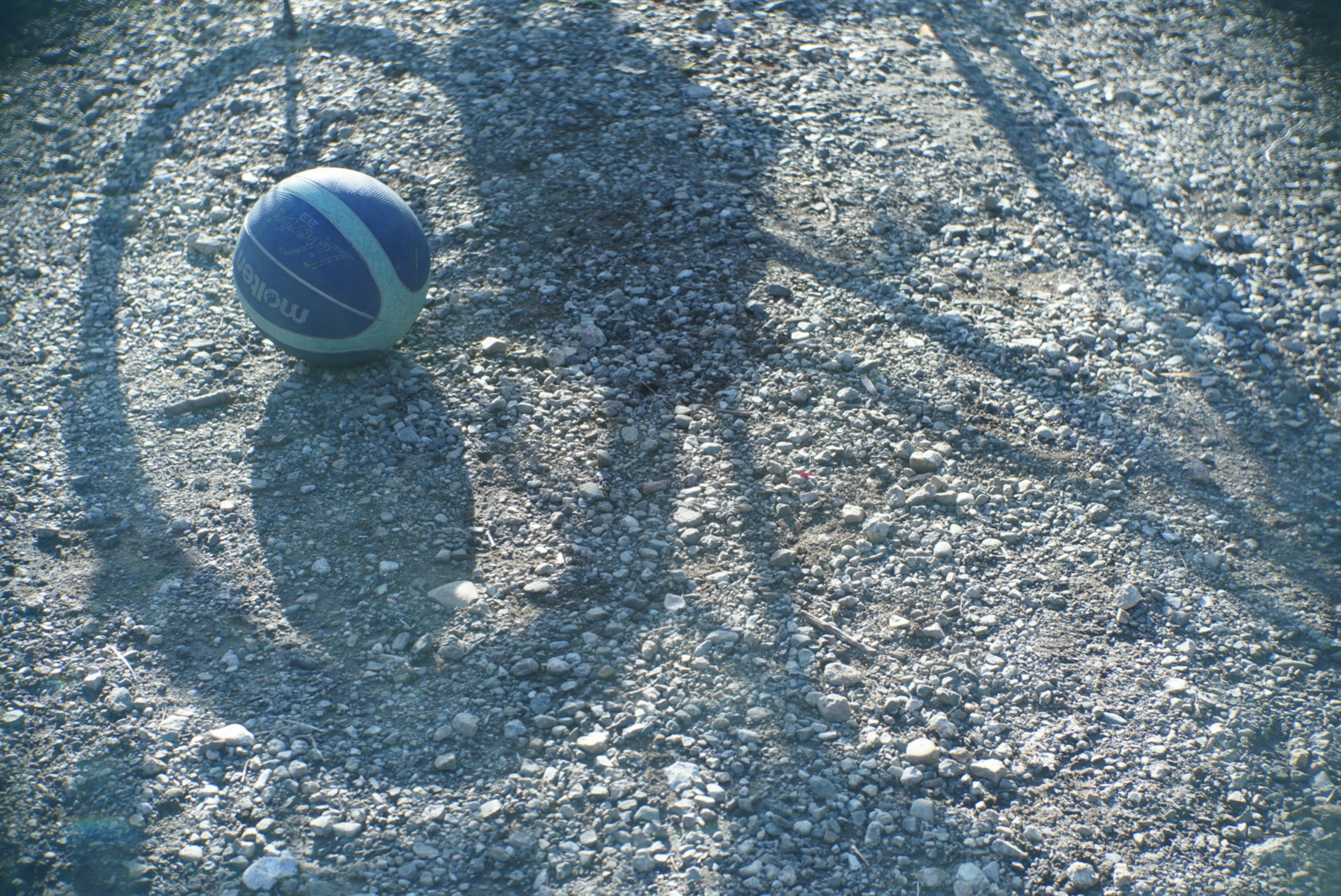 Ein blauer Basketball liegt auf Kies und wirft Schatten