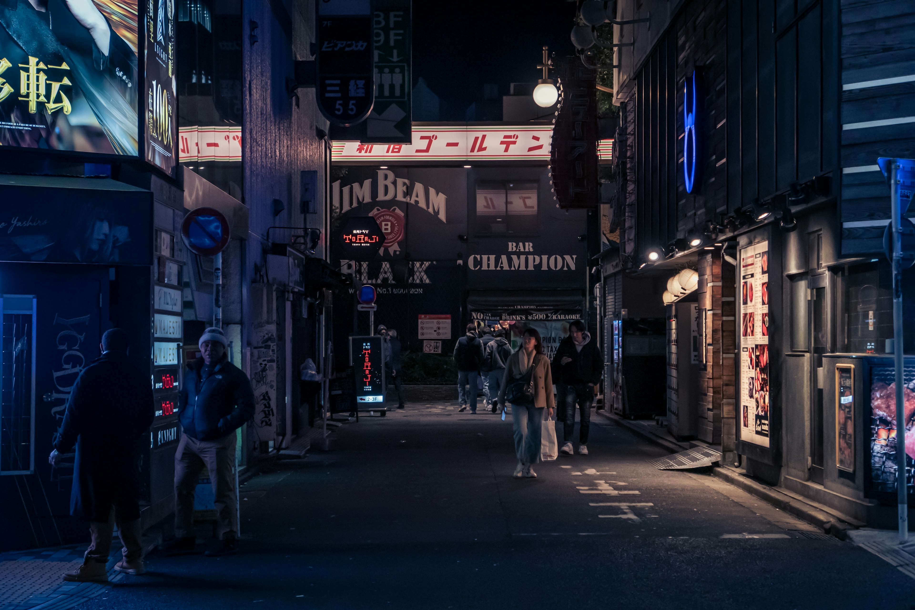 Dark street scene with people walking illuminated by neon signs at night