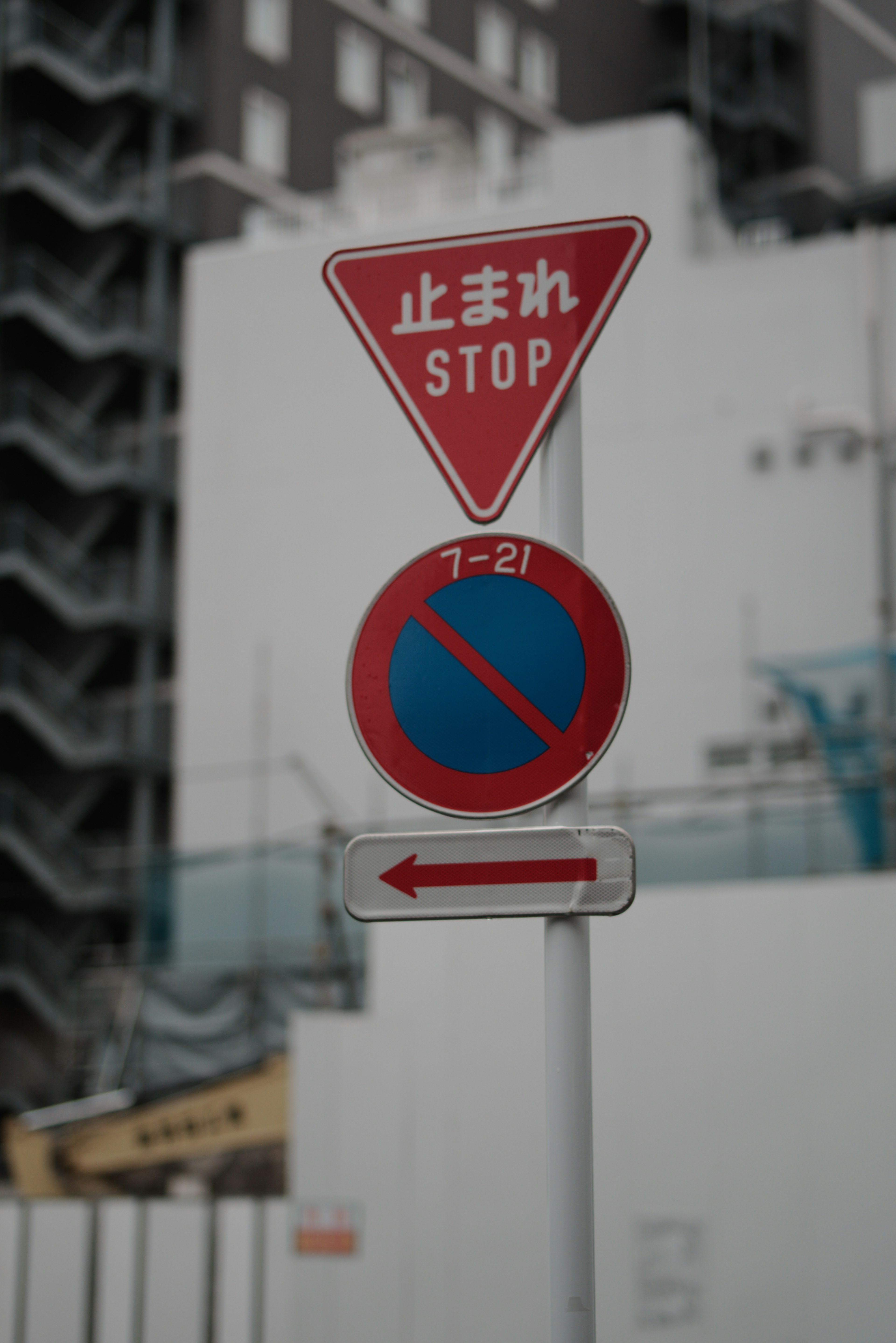 Señal de alto triangular roja con texto en japonés y señal de no estacionar azul