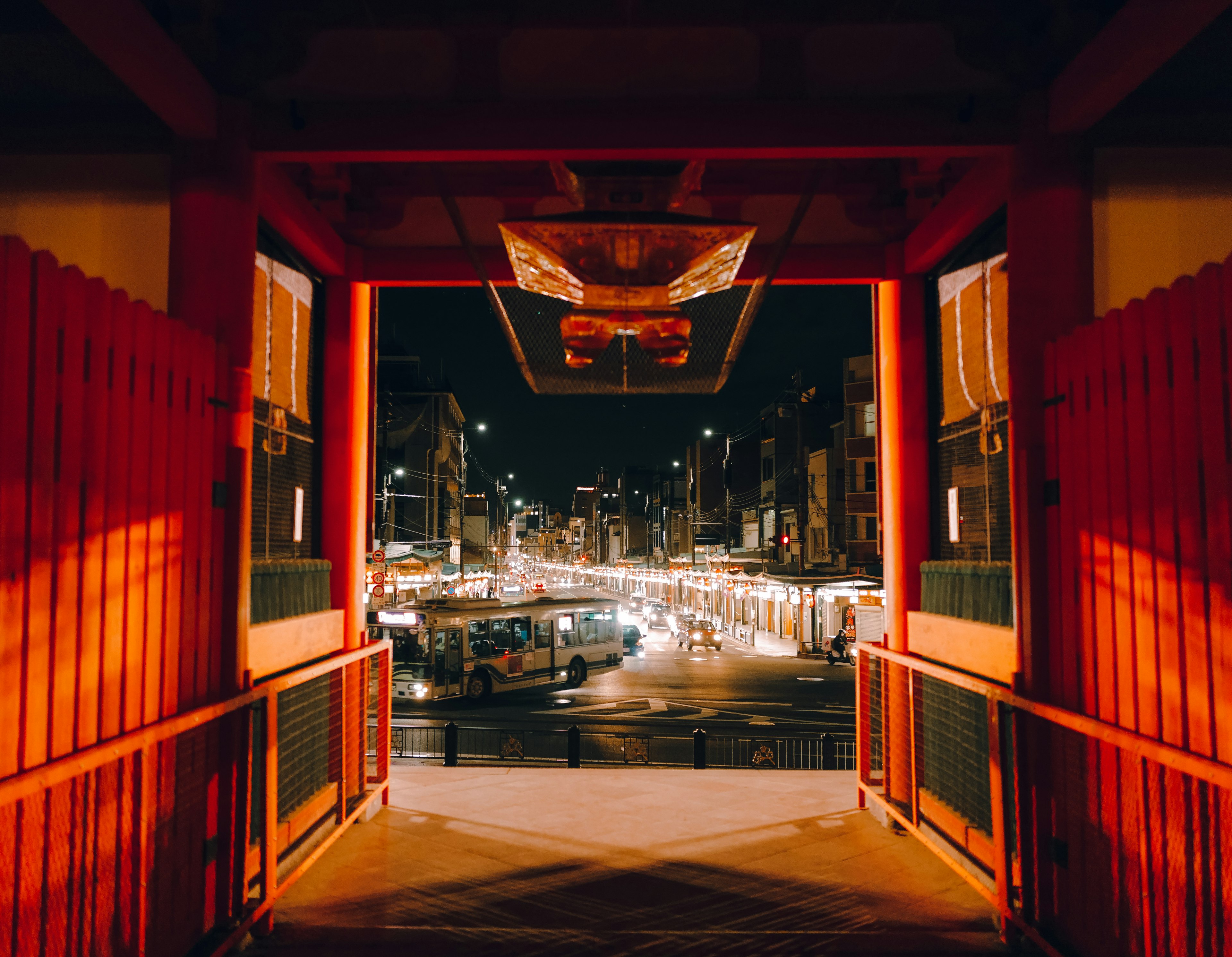 Vue à travers une porte rouge montrant une rue illuminée la nuit