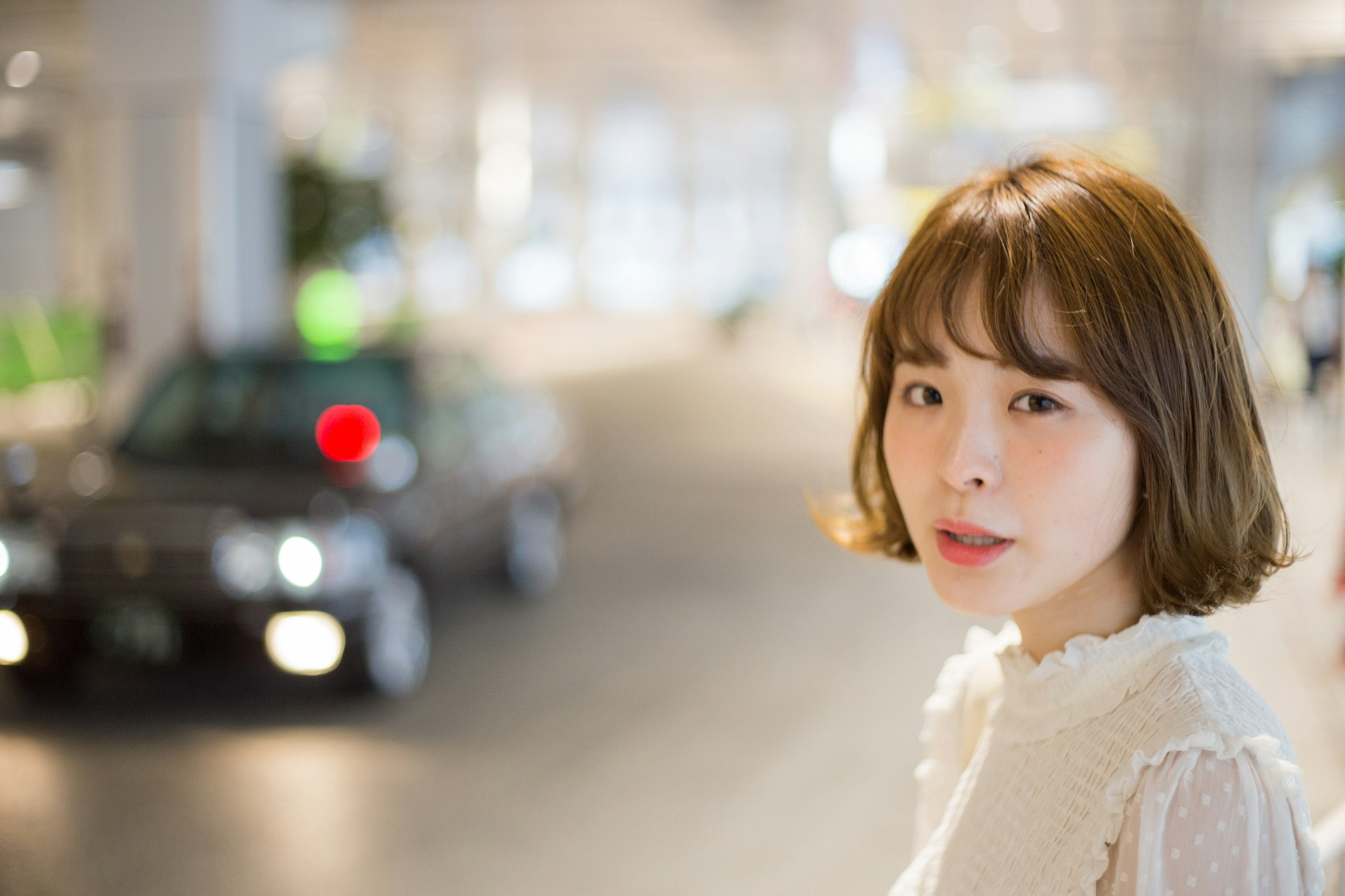 A woman smiling in the street with a blurred car and bright city background