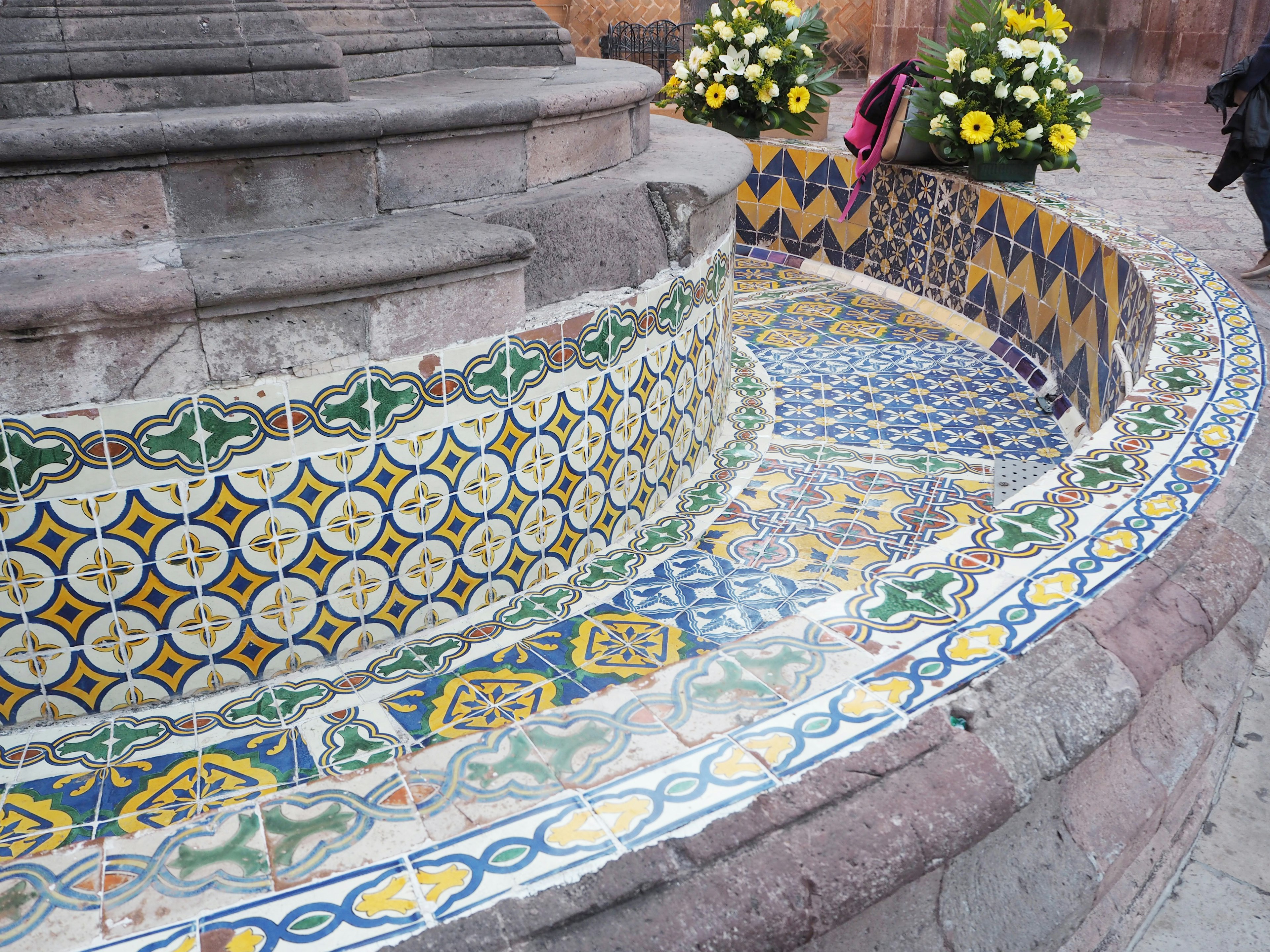 Elemento de agua curvo con decoraciones de azulejos vibrantes y flores amarillas cercanas