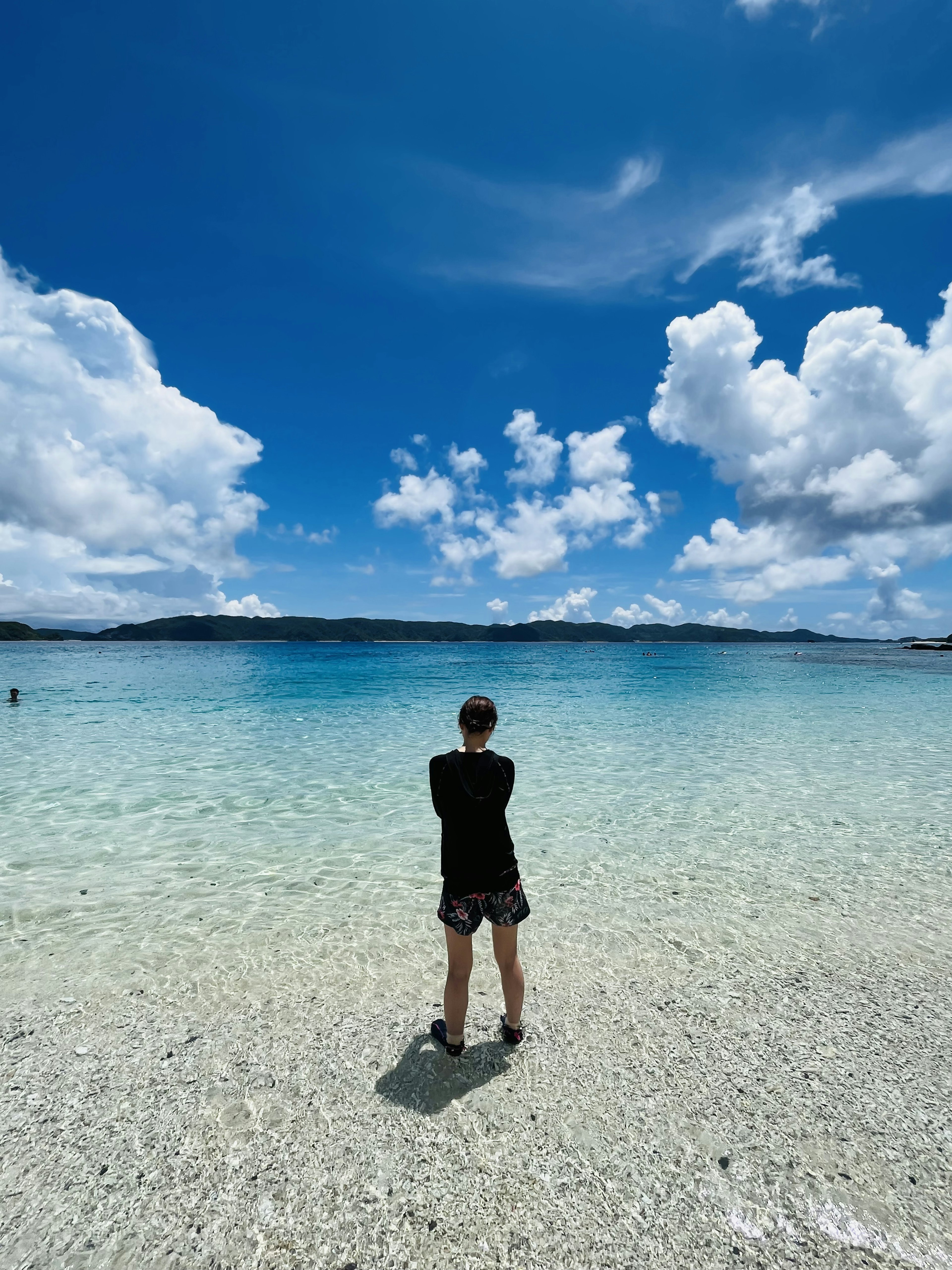 Person standing in clear water under a blue sky with fluffy clouds