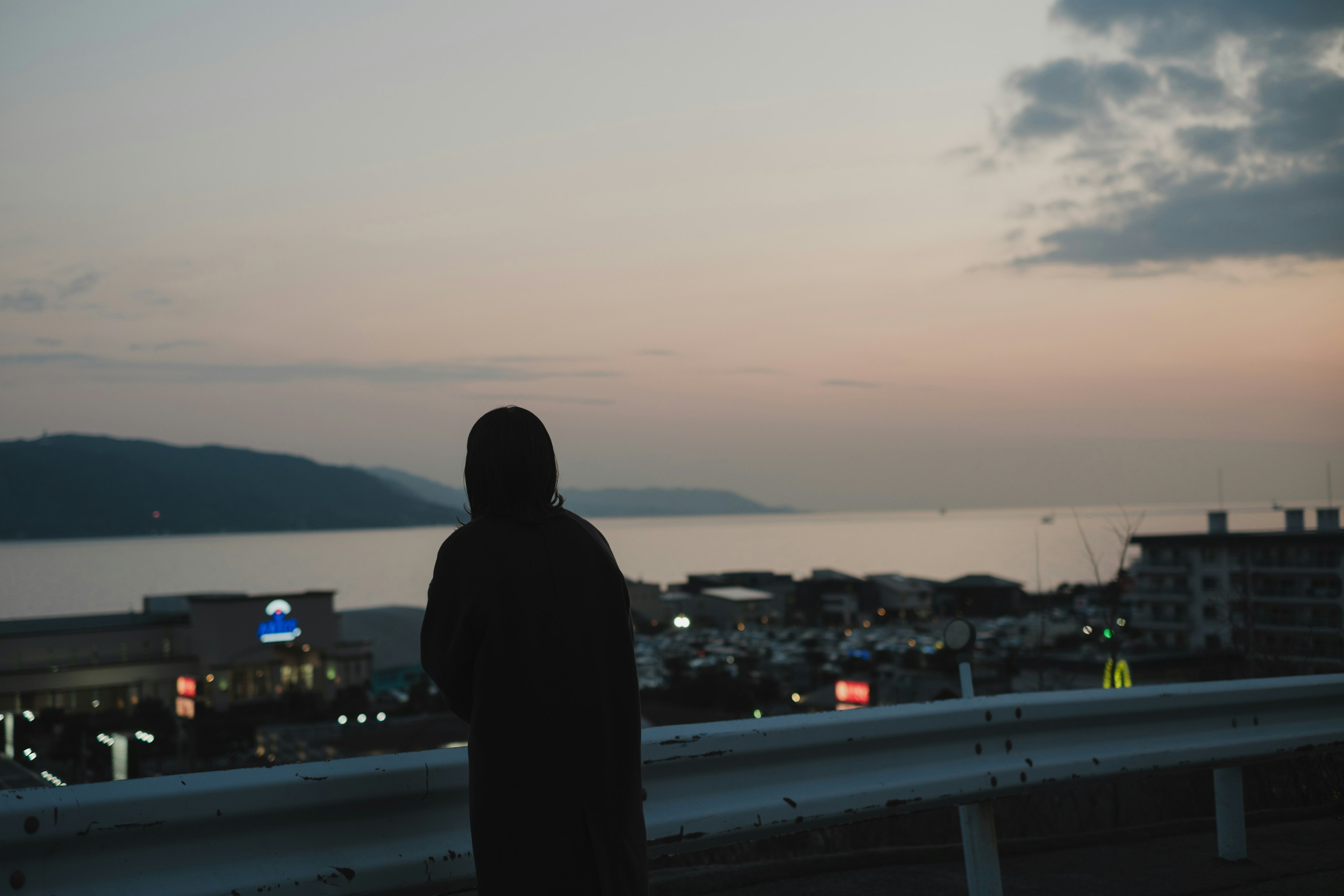 海を見つめる黒いフードをかぶった人物のシルエットと夕焼けの風景