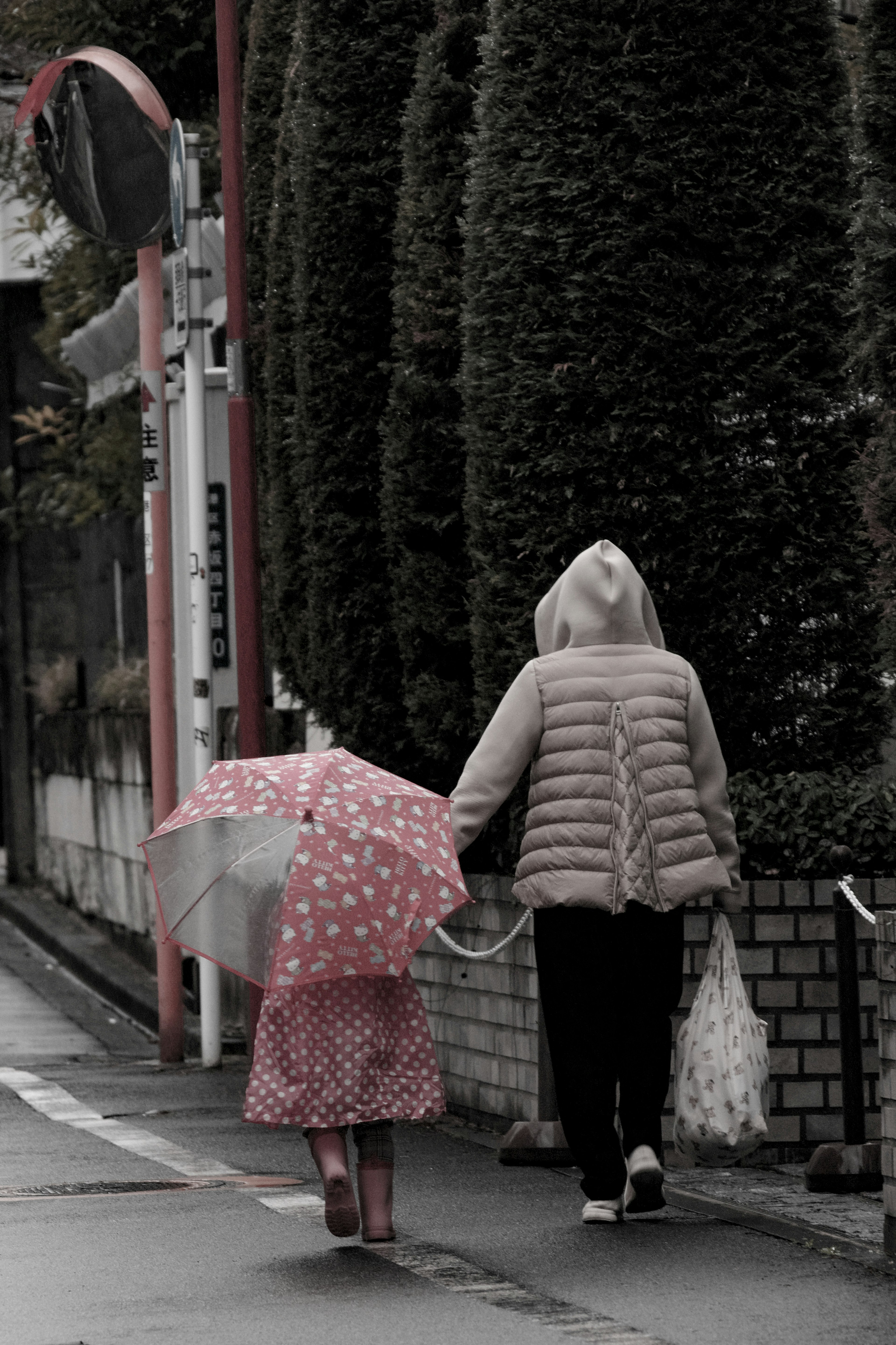 Ein Kind mit einem gepunkteten Regenschirm, das mit einem Erwachsenen in einer gepolsterten Jacke geht