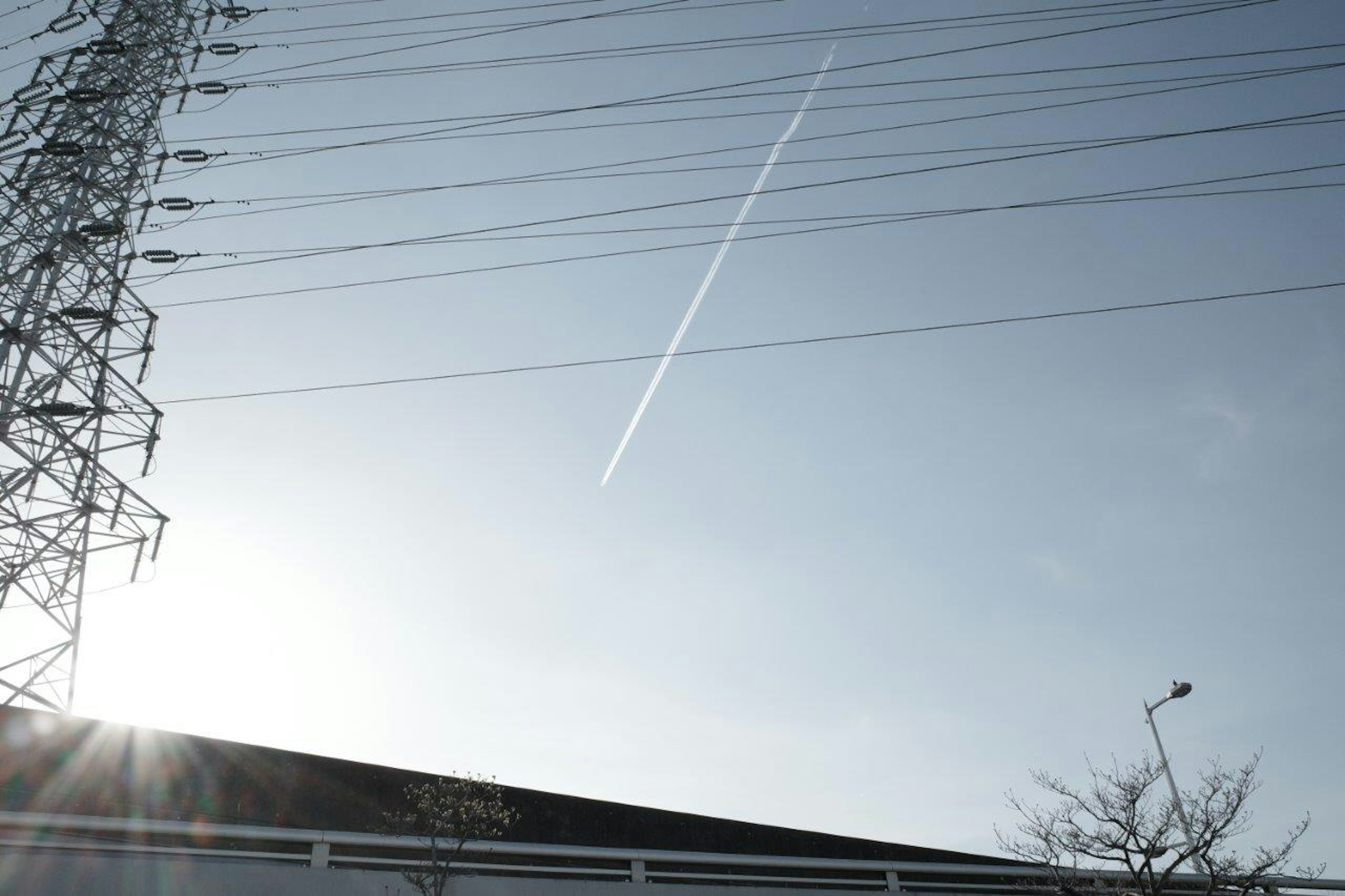 晴れた空に電線と飛行機雲が見える風景