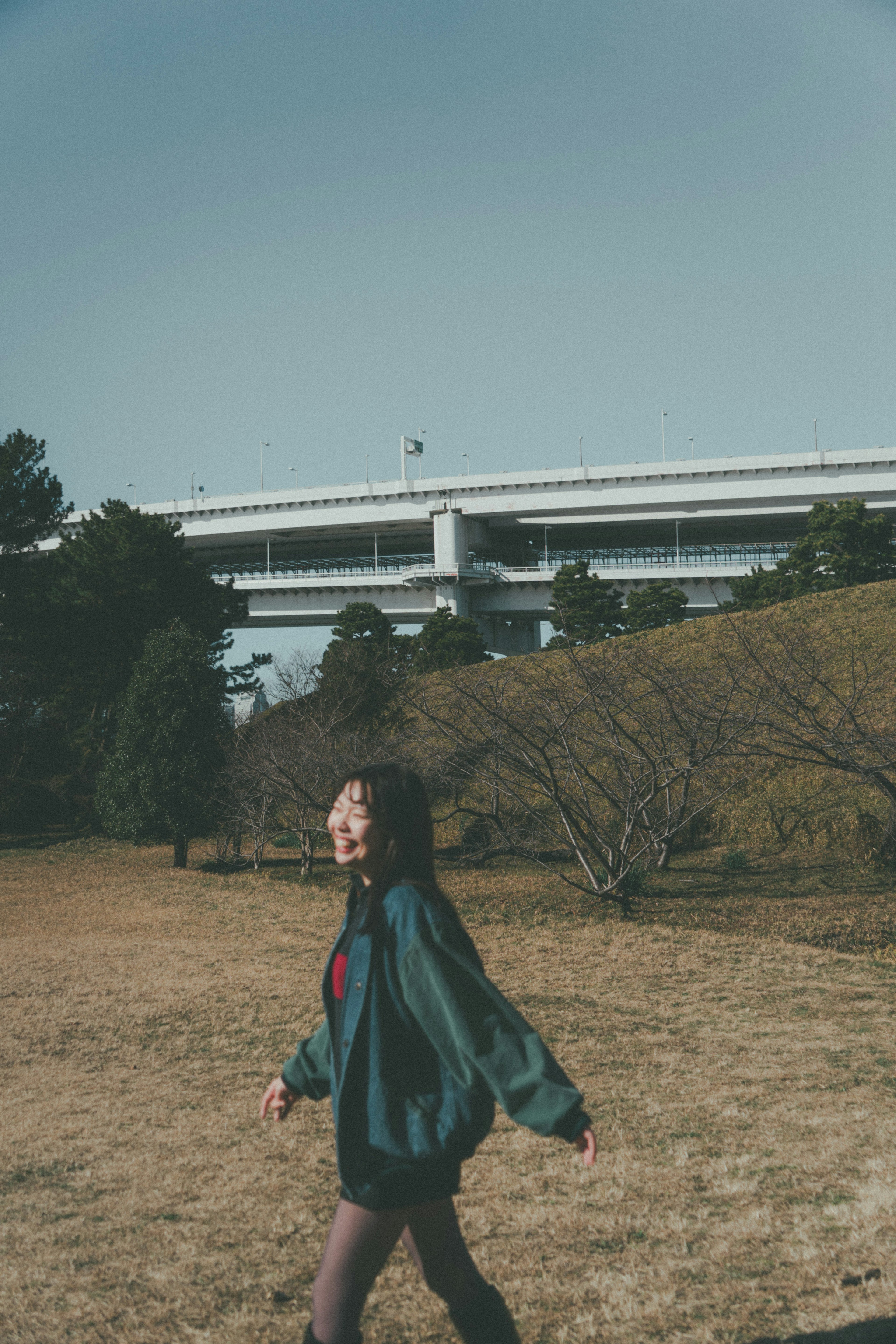 A woman walking in a park with an elevated highway in the background