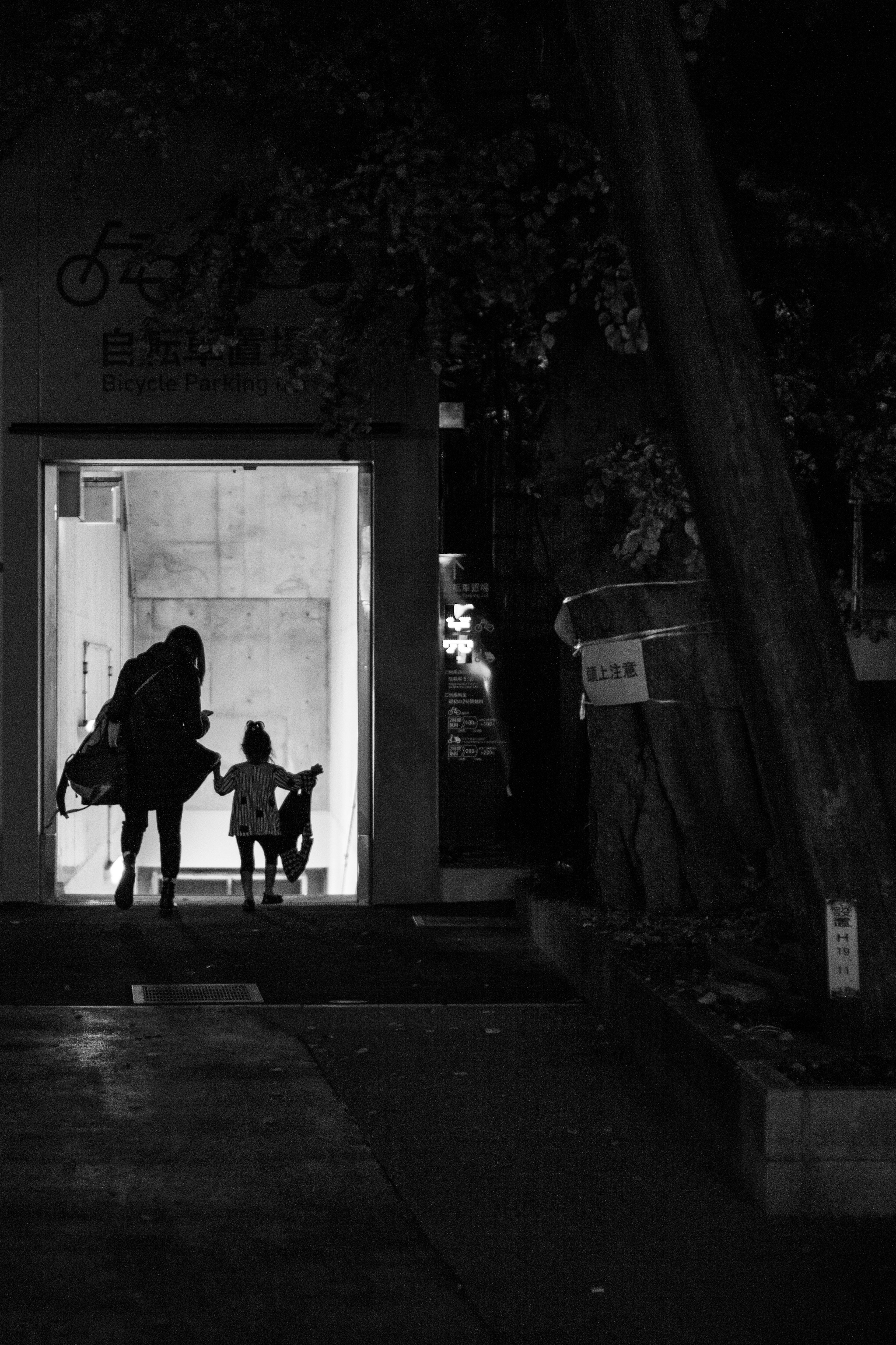 Siluet orang tua dan anak di depan pintu masuk yang terang dengan latar belakang gelap