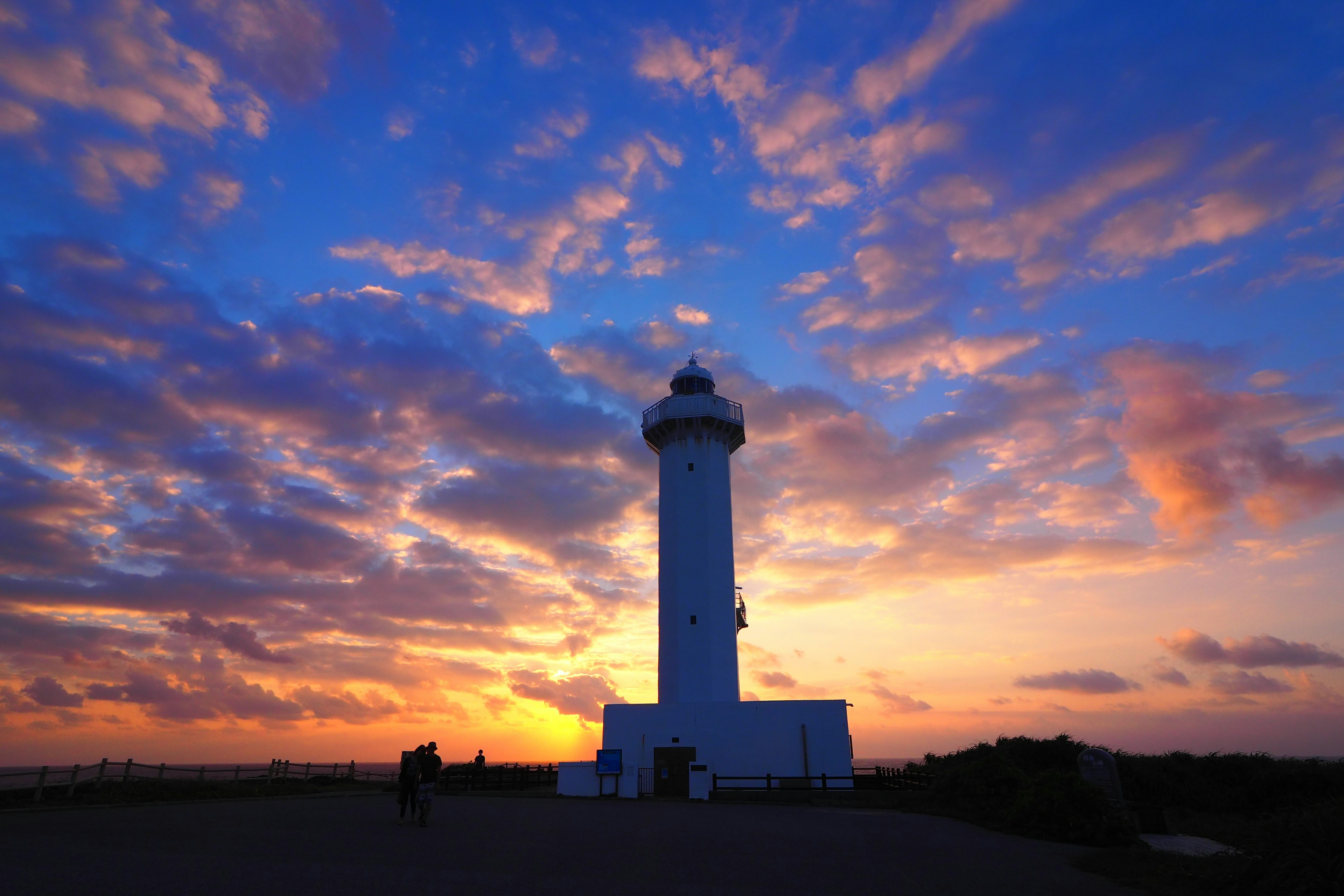 Silueta de un faro blanco contra un cielo de atardecer colorido