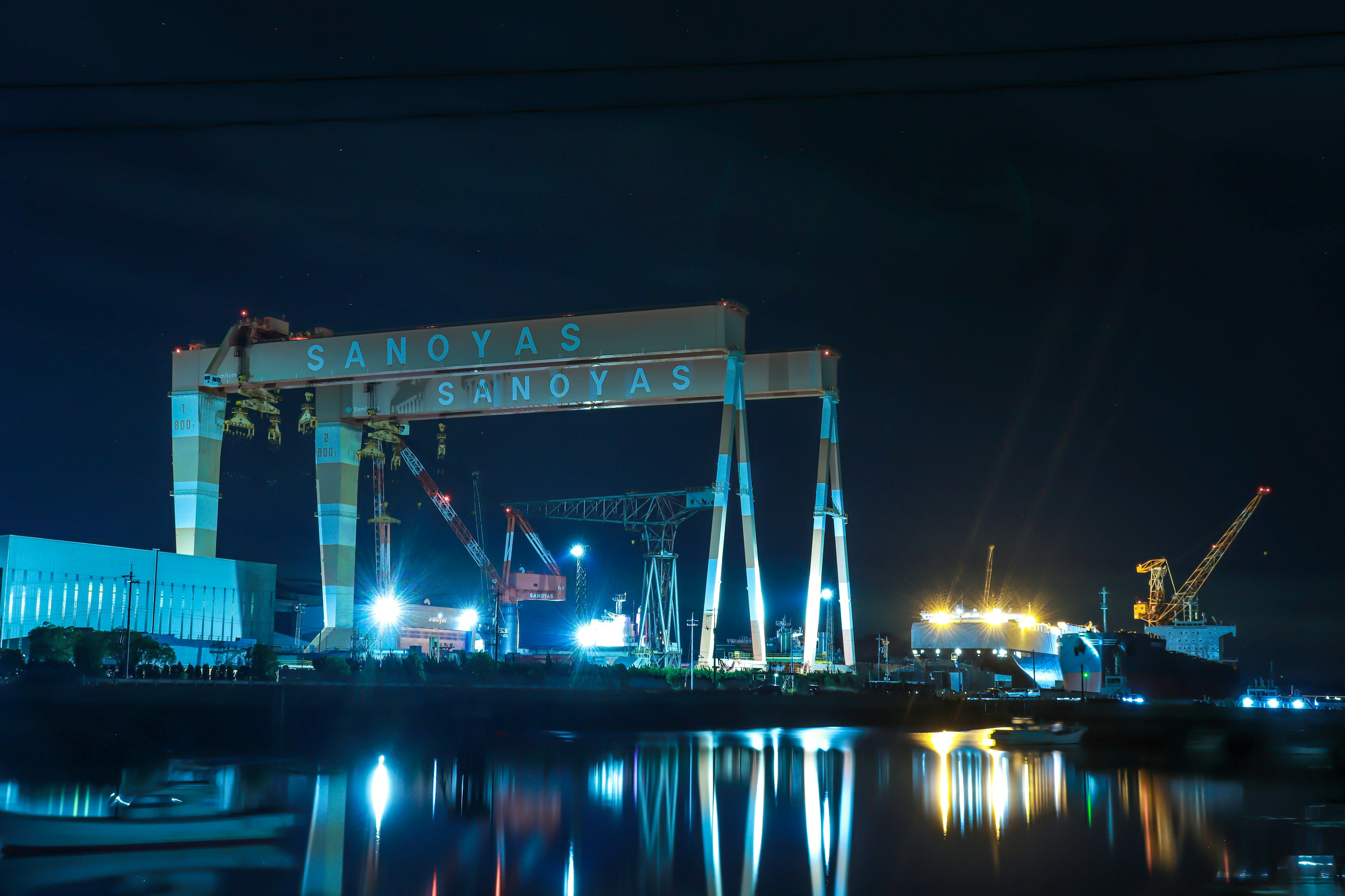 Große Kräne bei Nacht im Hafen beleuchtet mit Spiegelungen im Wasser