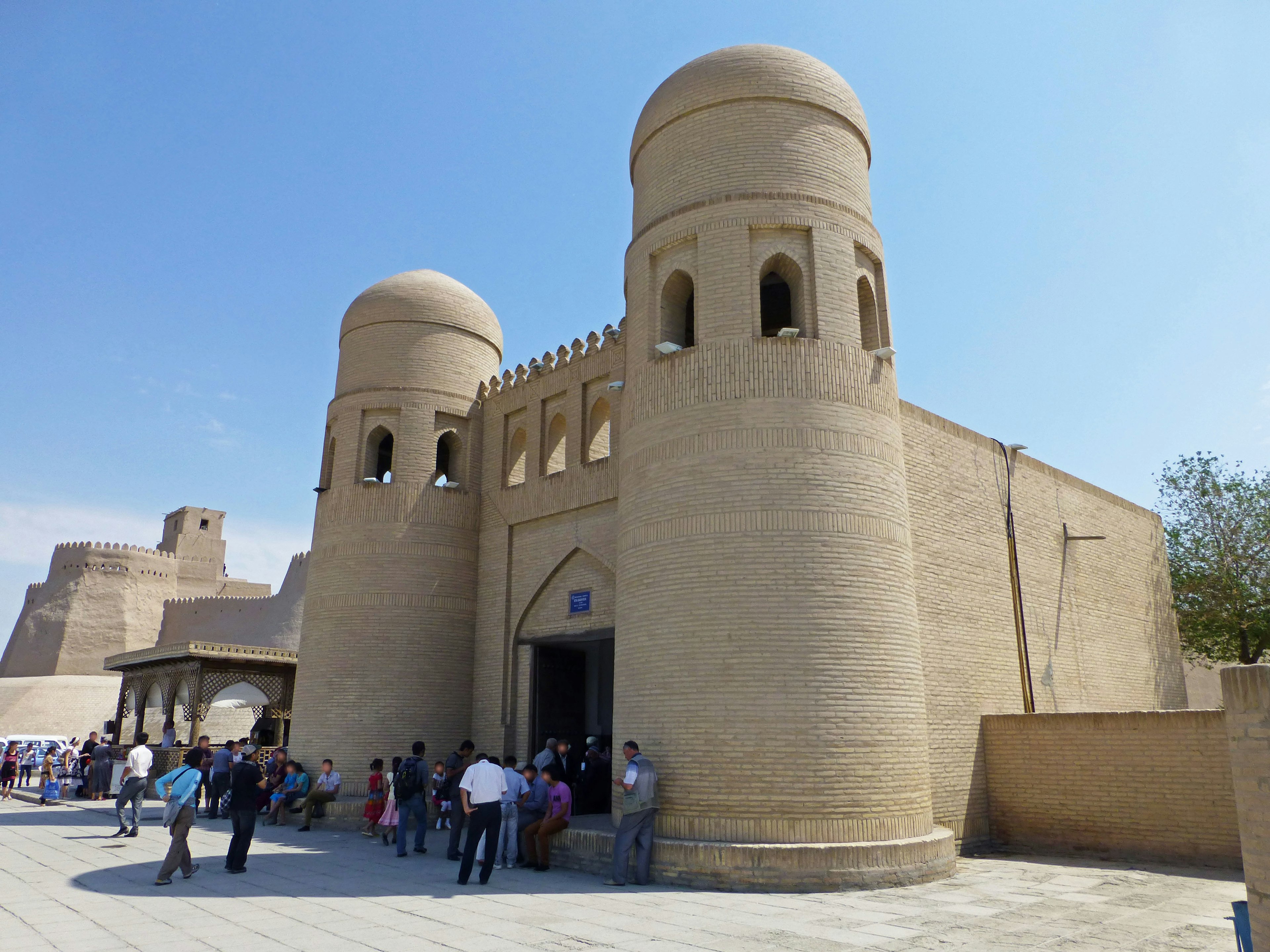 Edificio histórico de barro con torres y visitantes