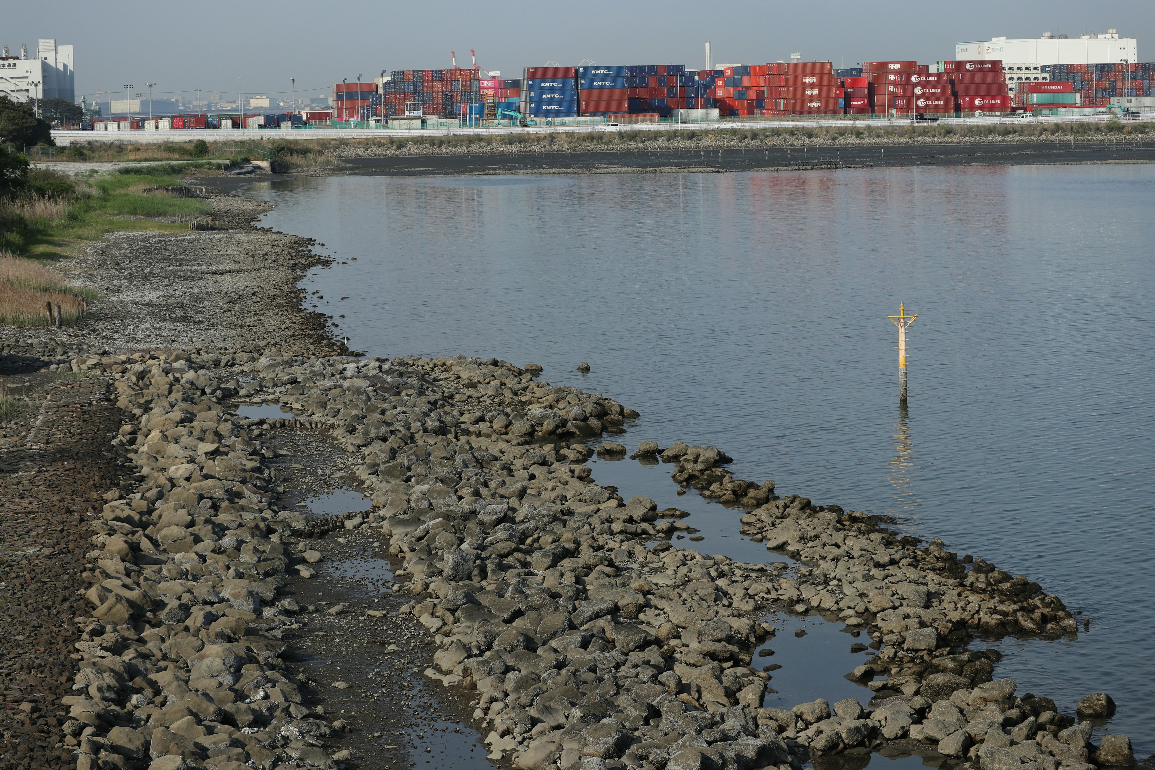 Rocks along the riverbank with colorful shipping containers in the background