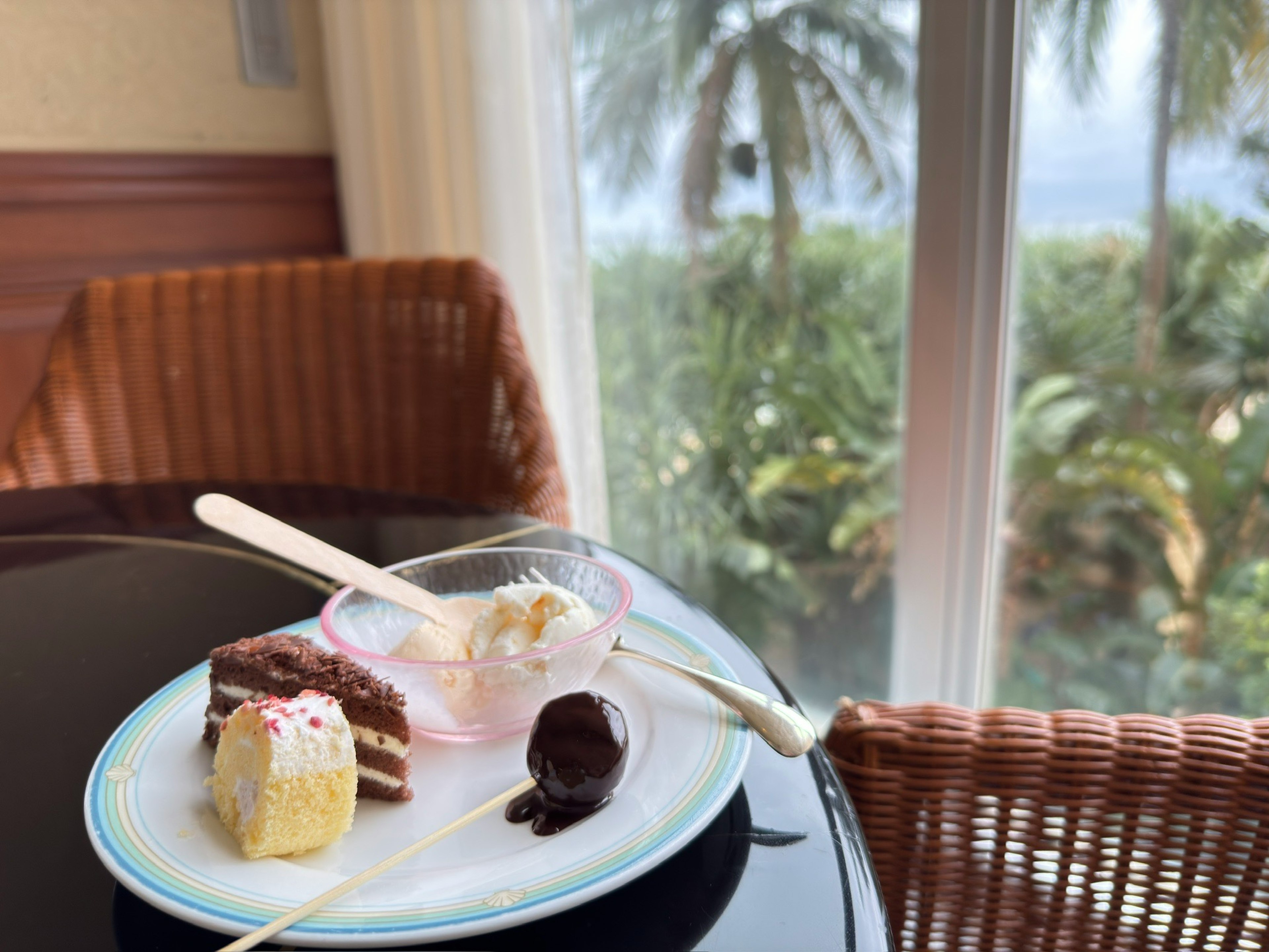 Assiette de dessert sur une table avec gâteau et glace, palmiers visibles en arrière-plan