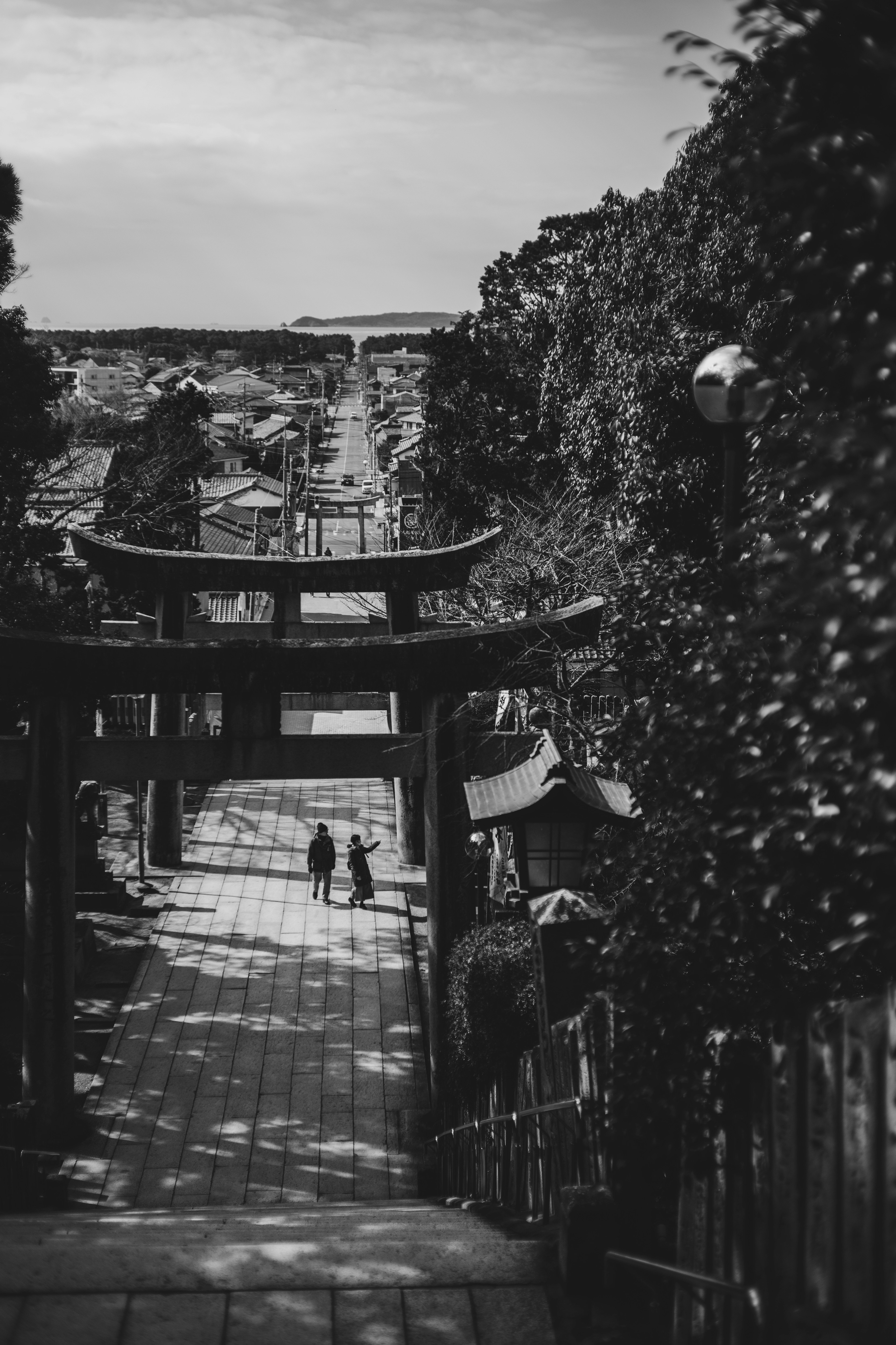 Immagine in bianco e nero di un torii e due persone che scendono scale di pietra