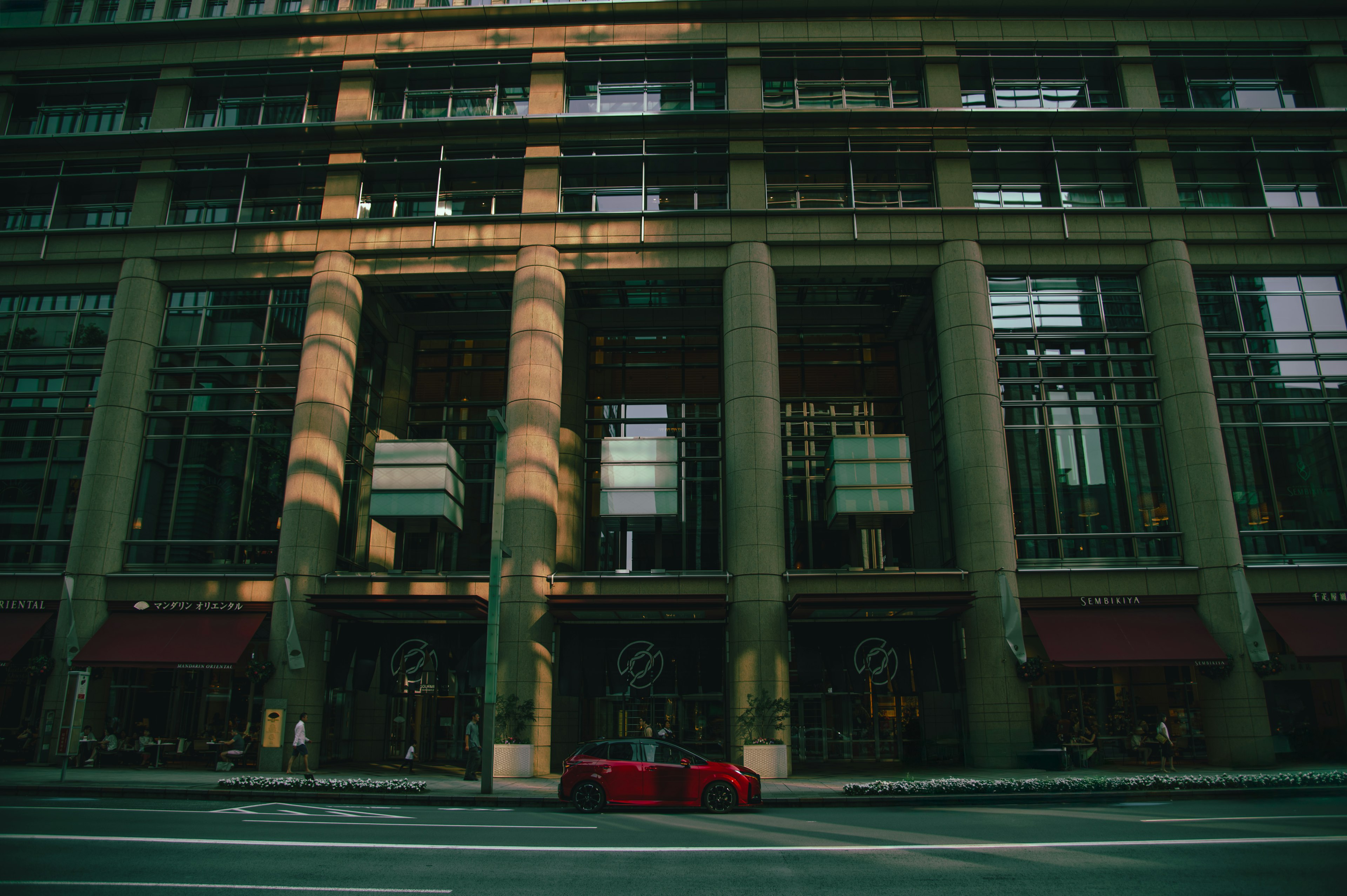 Façade d'un bâtiment moderne avec une voiture rouge garée devant mettant en avant des éclairages et des ombres uniques