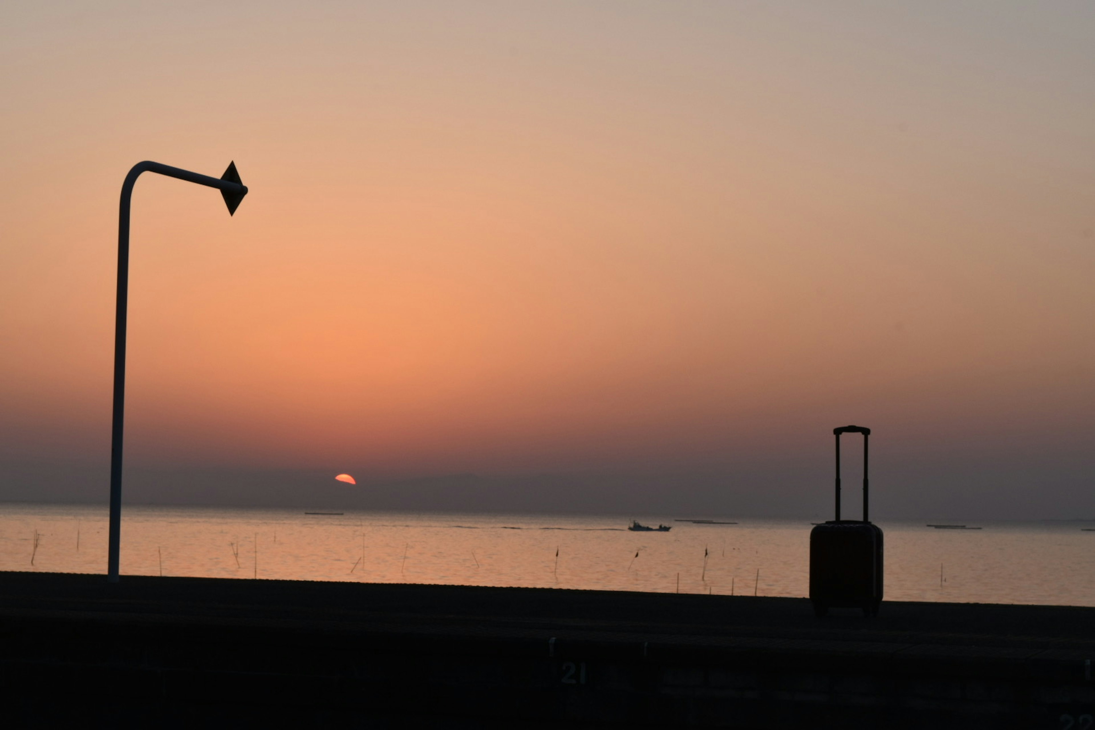 Sonnenuntergang über dem Meer mit einer Straßenlaterne und einem Koffer im Bild