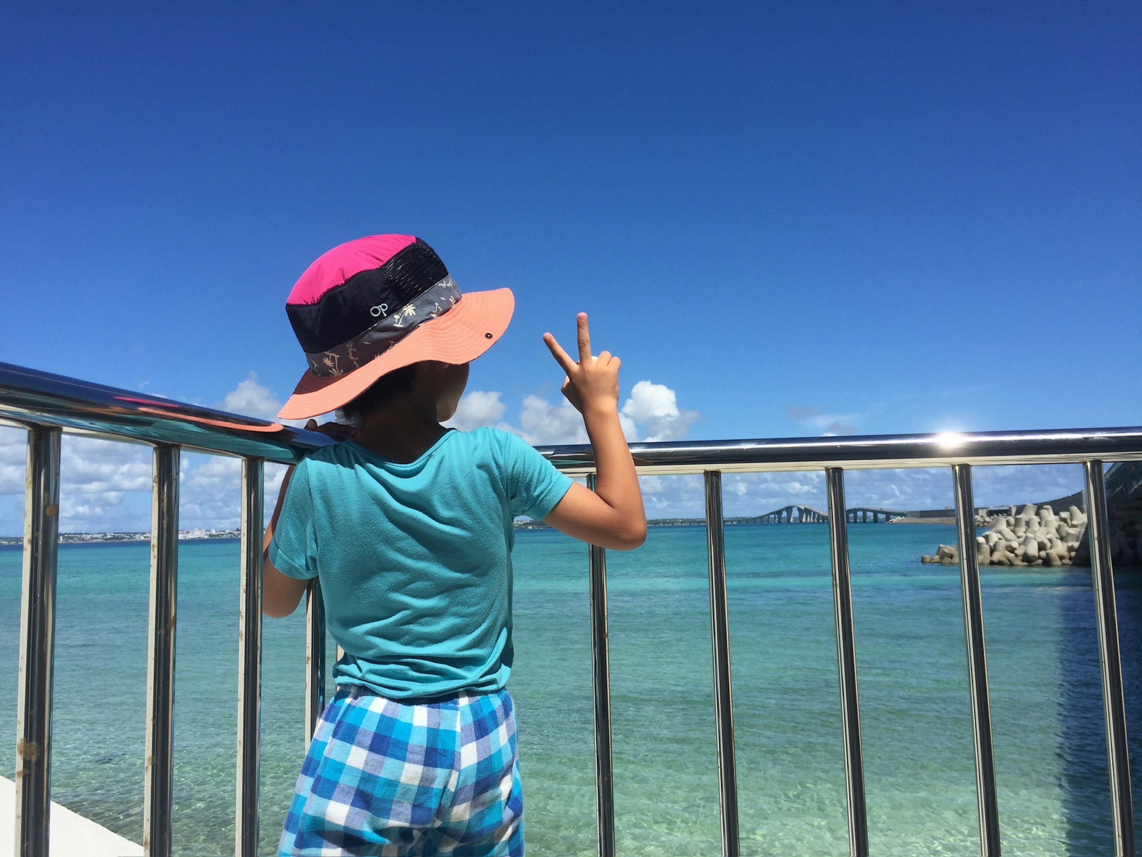 Un niño con un sombrero haciendo un signo de paz frente a un fondo de mar azul