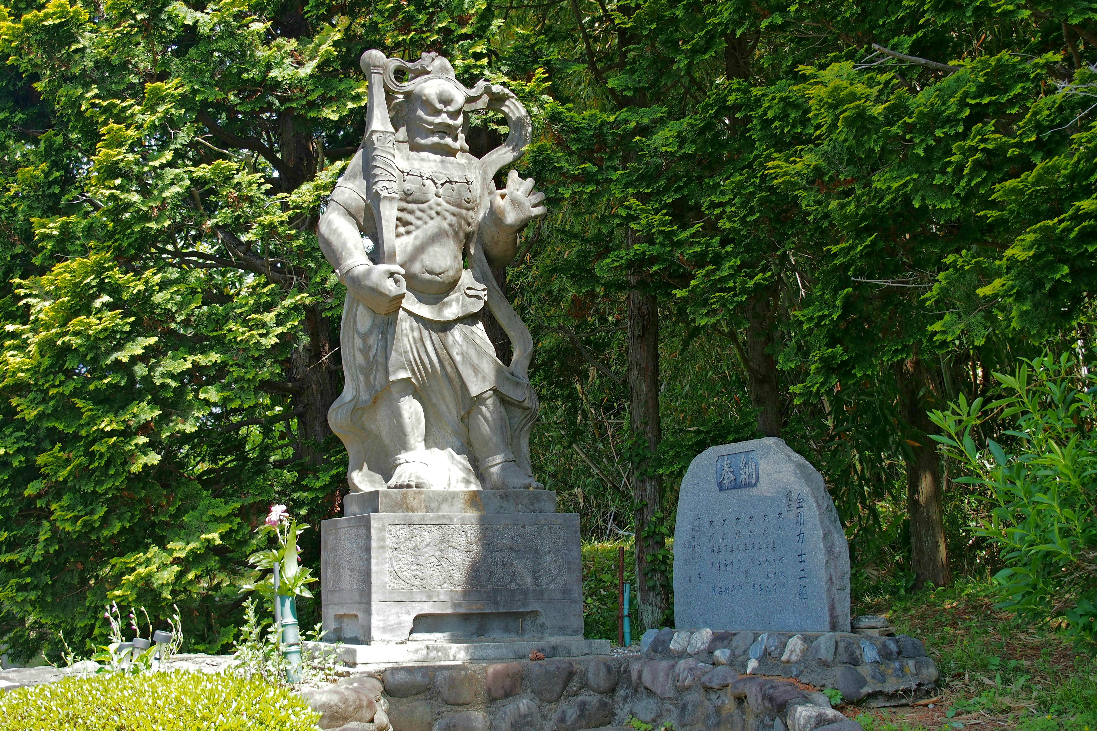 A stone statue of a deity standing in a lush green setting