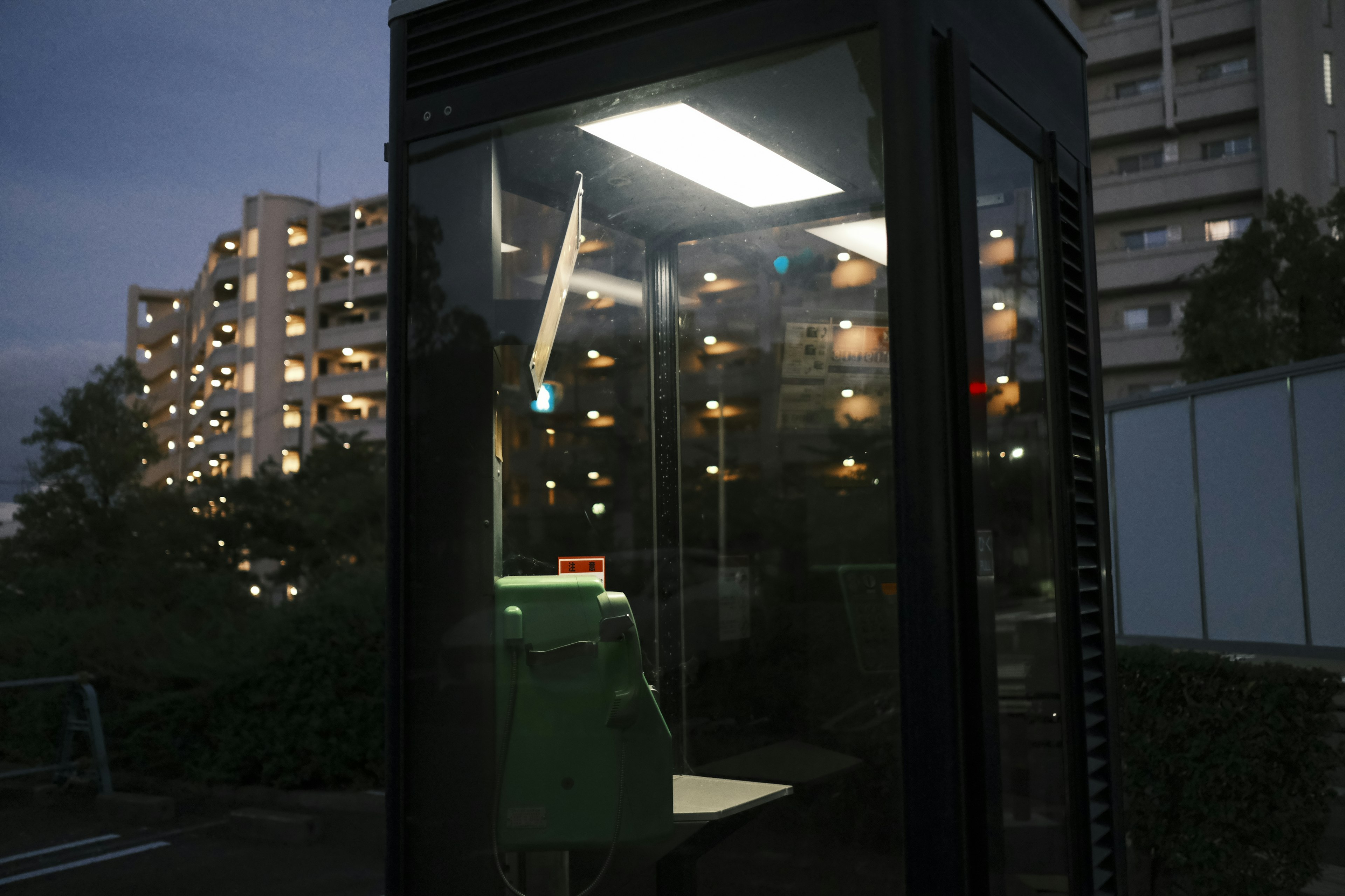 Public telephone booth at night with illuminated apartment buildings in the background