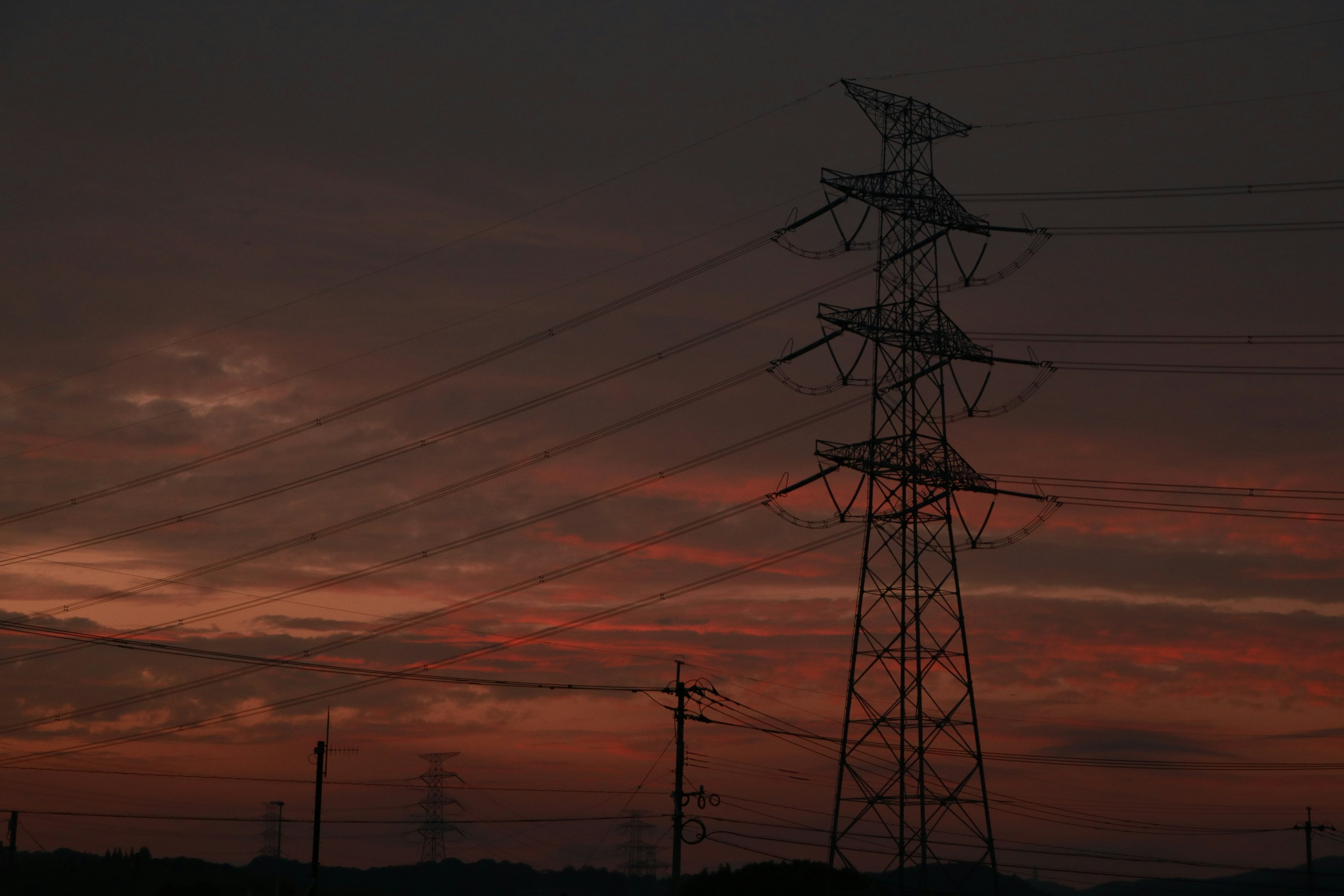 Silhouette of power lines and pylons against a sunset