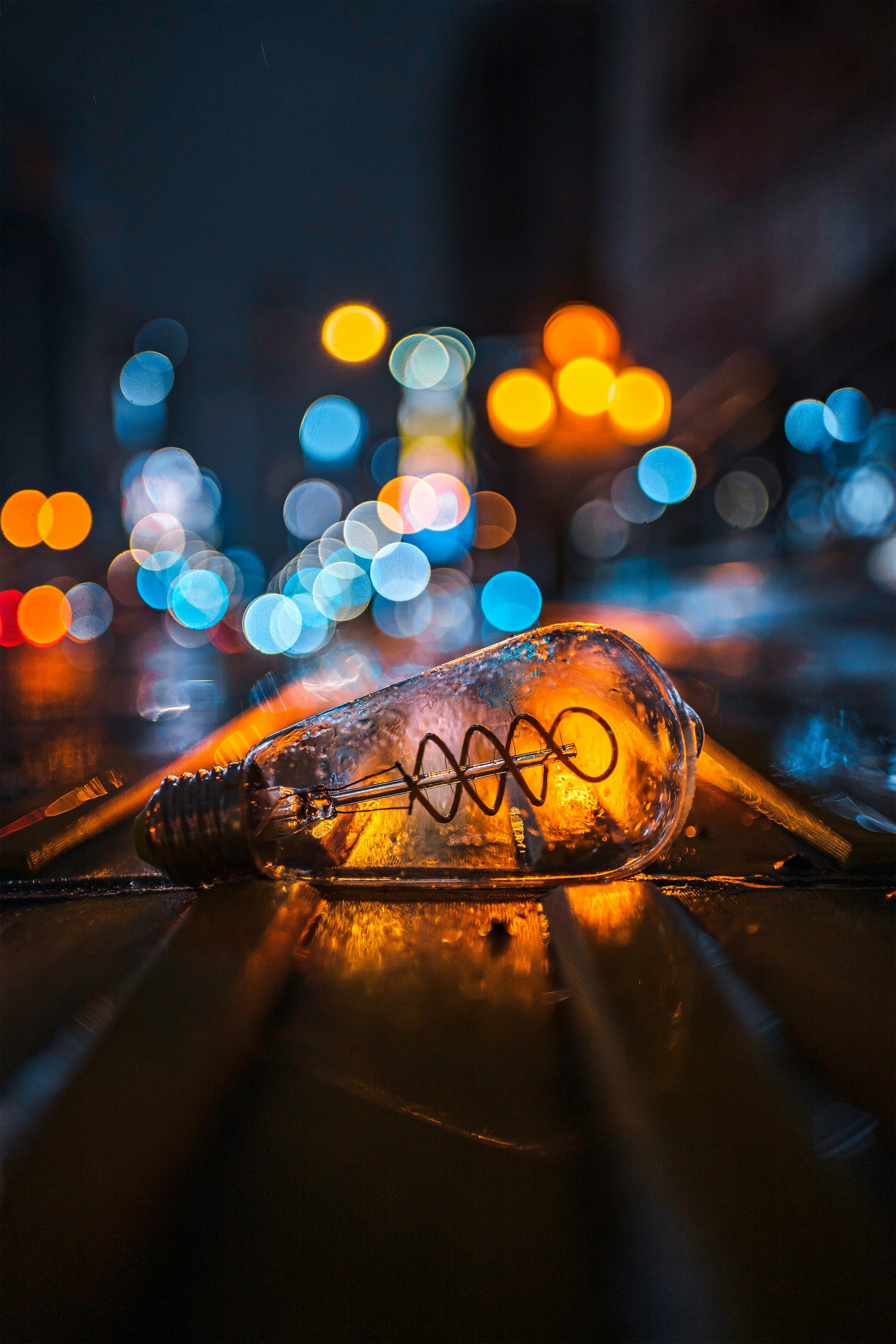 A fallen light bulb on a wet street at night with blurred colorful lights in the background