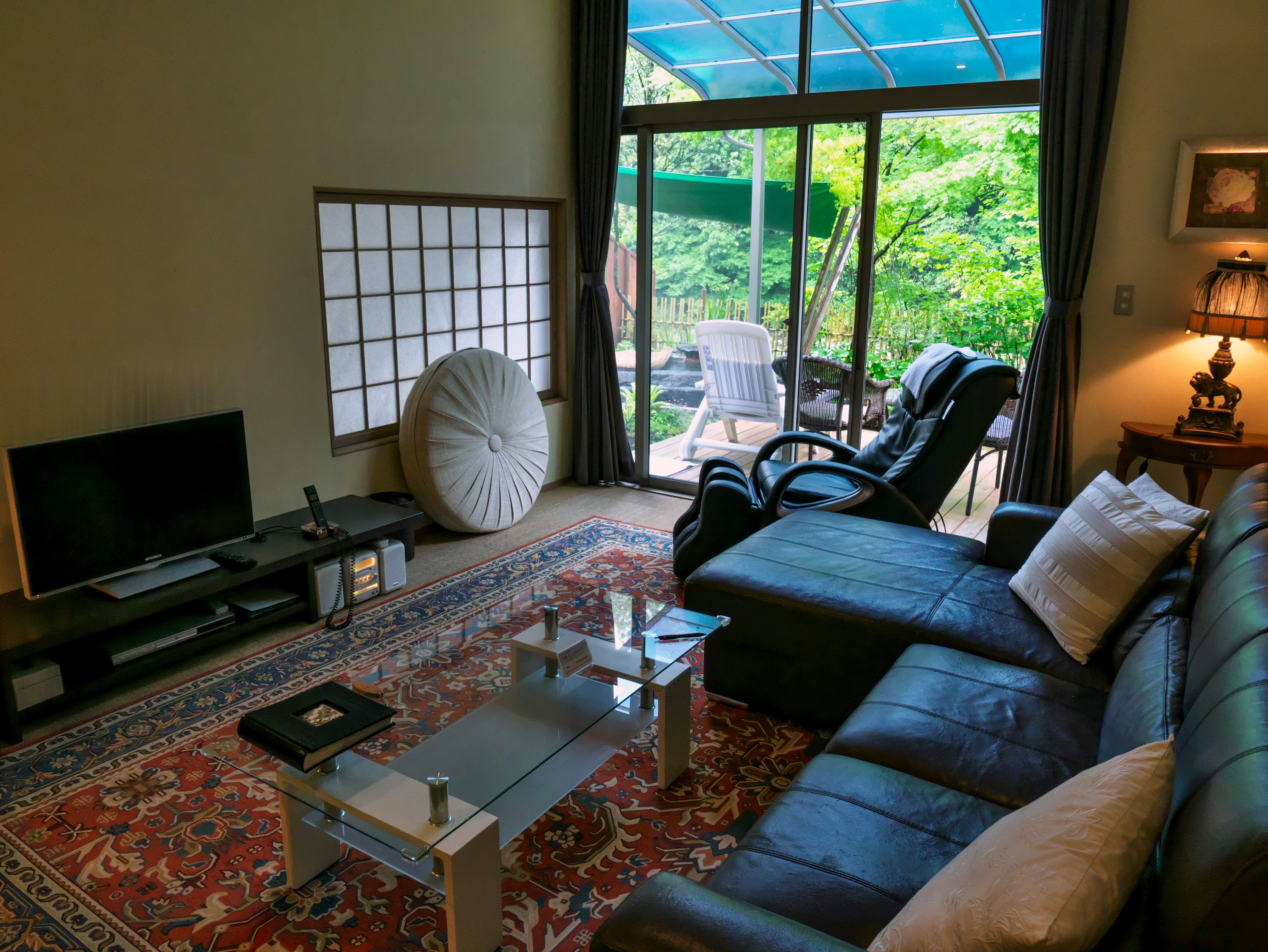 Cozy living room with a leather sofa coffee table and large windows overlooking greenery