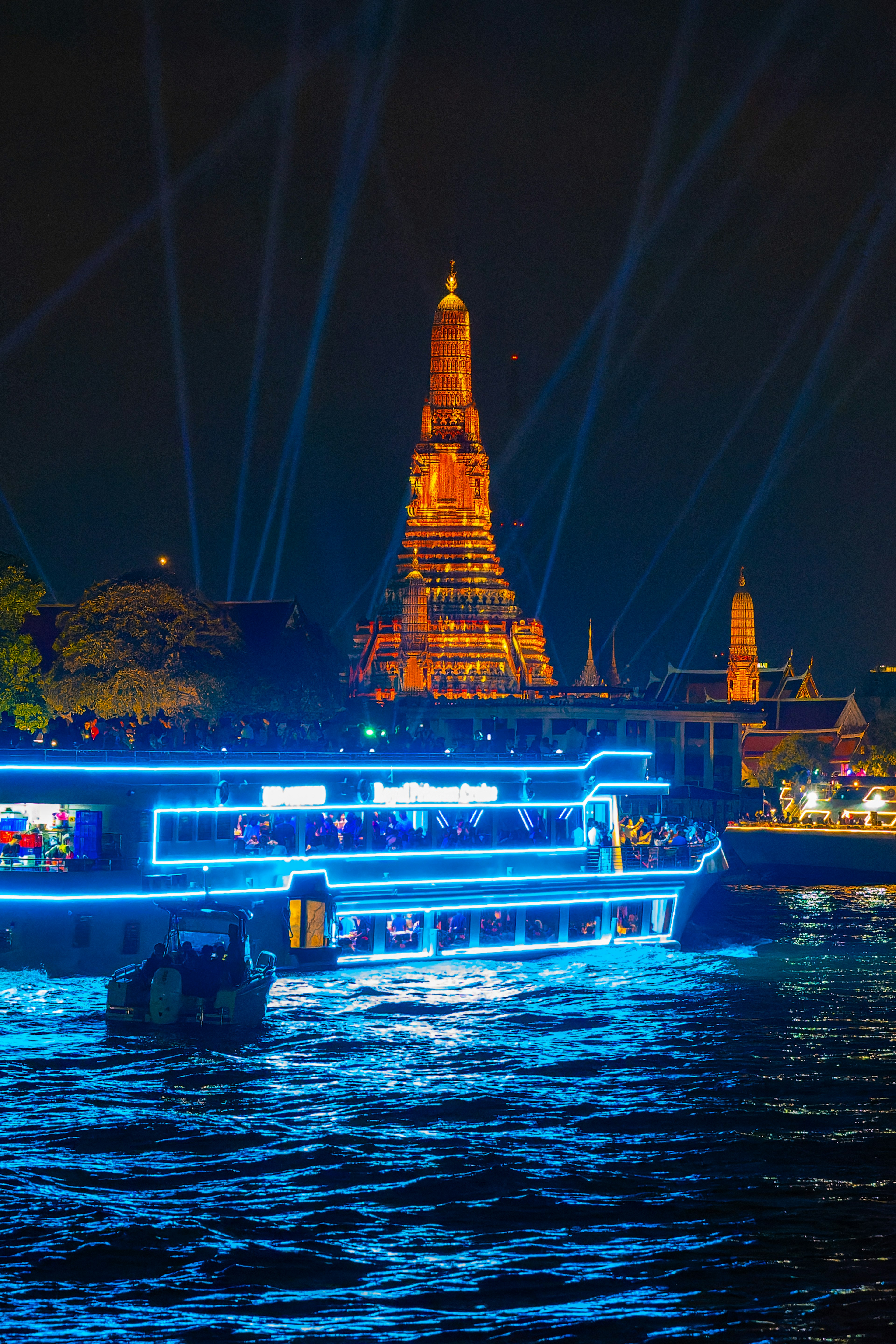 Wat Arun illuminated at night with a blue-lit boat on the river