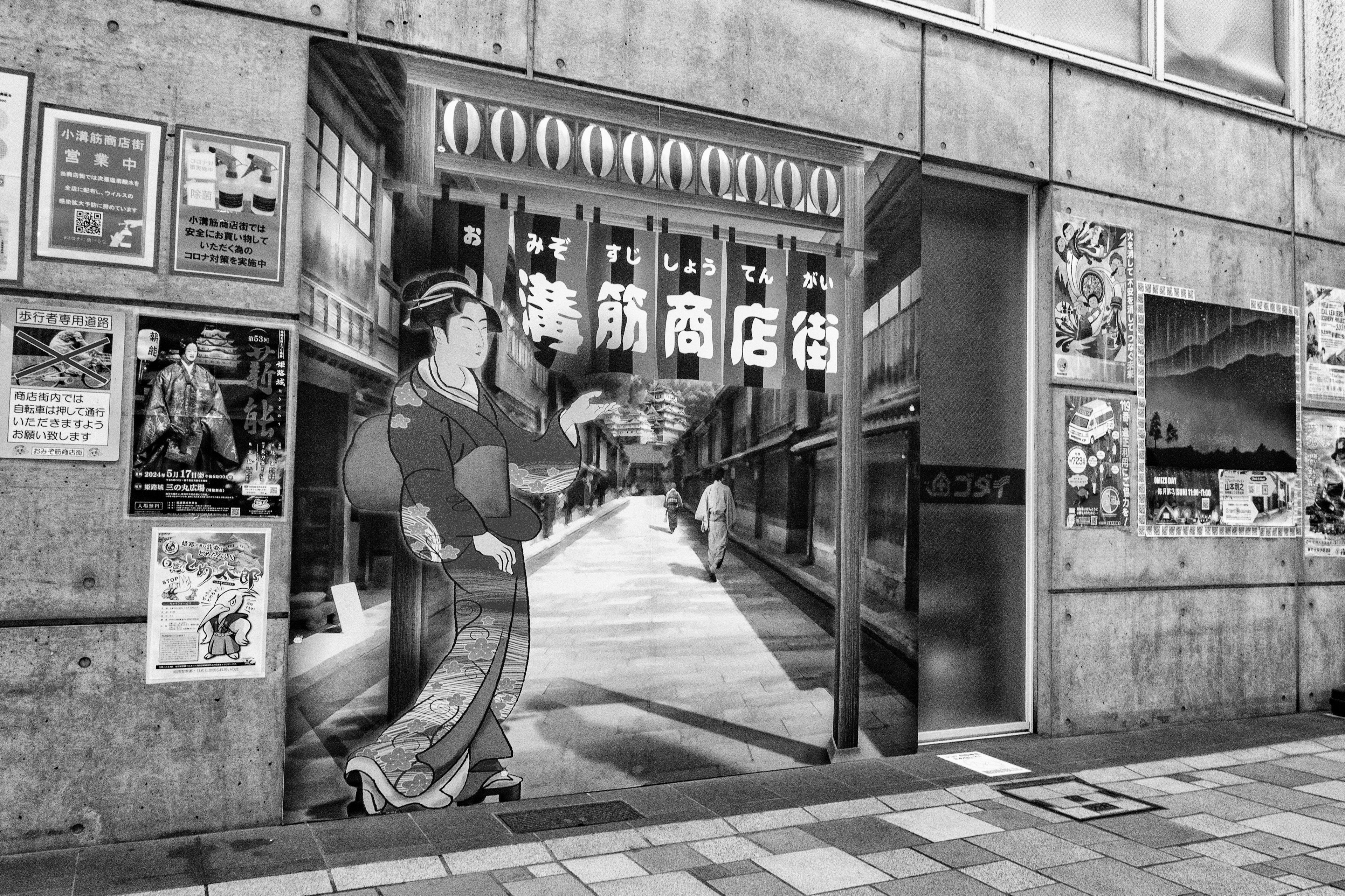 Murale in bianco e nero di una donna in kimono all'ingresso di una via dello shopping