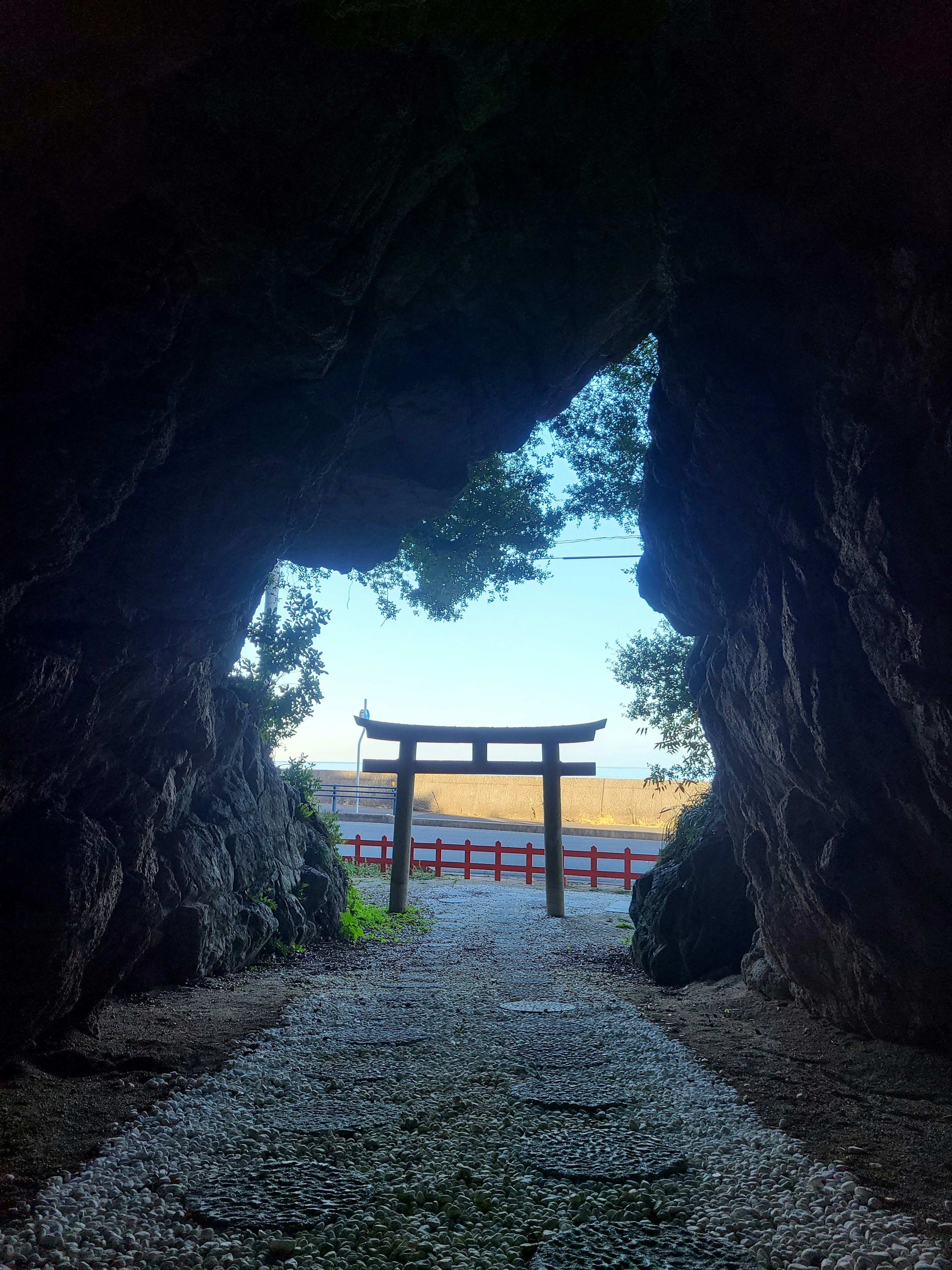 Blick auf ein Torii, das von einer Höhlenöffnung und blauem Himmel umrahmt ist