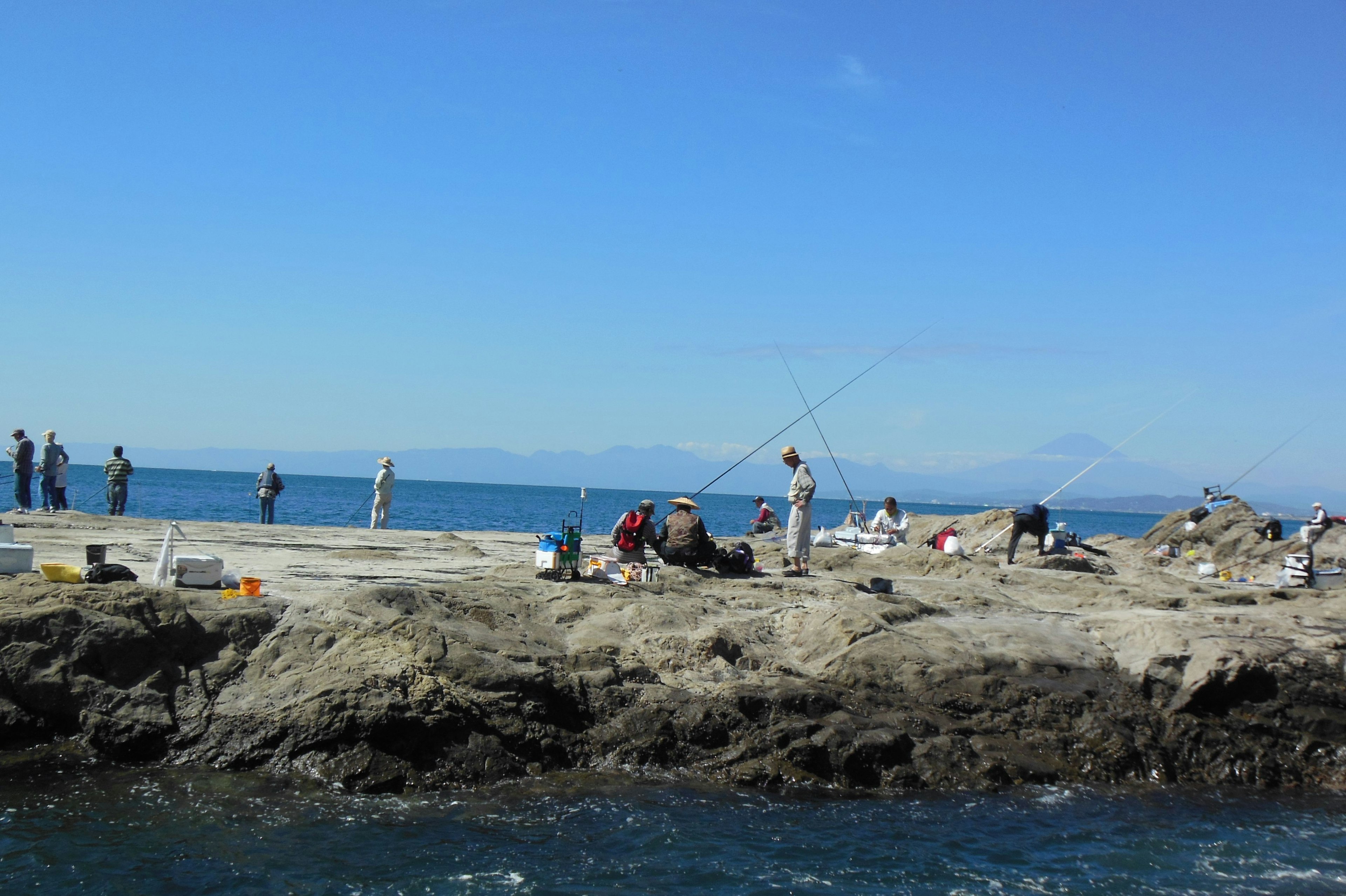 People fishing on a rocky shore under a clear blue sky