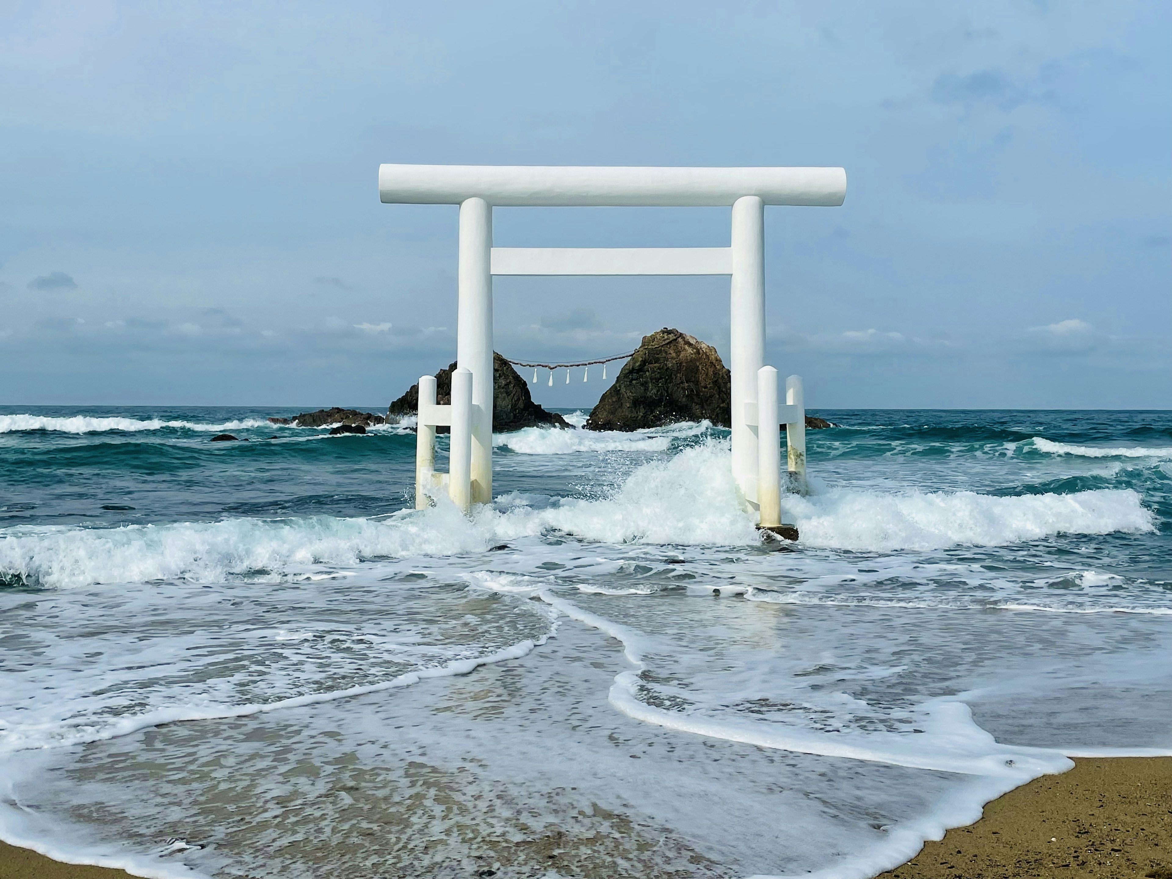 波の中に立つ白い鳥居と岩