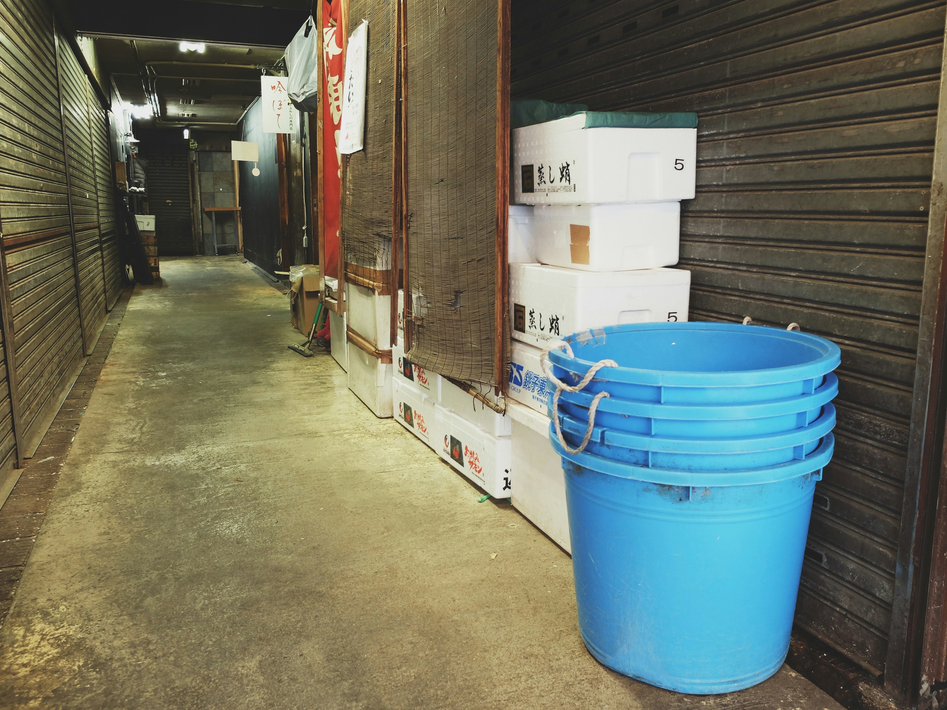 Narrow hallway with stacked boxes and a blue bucket