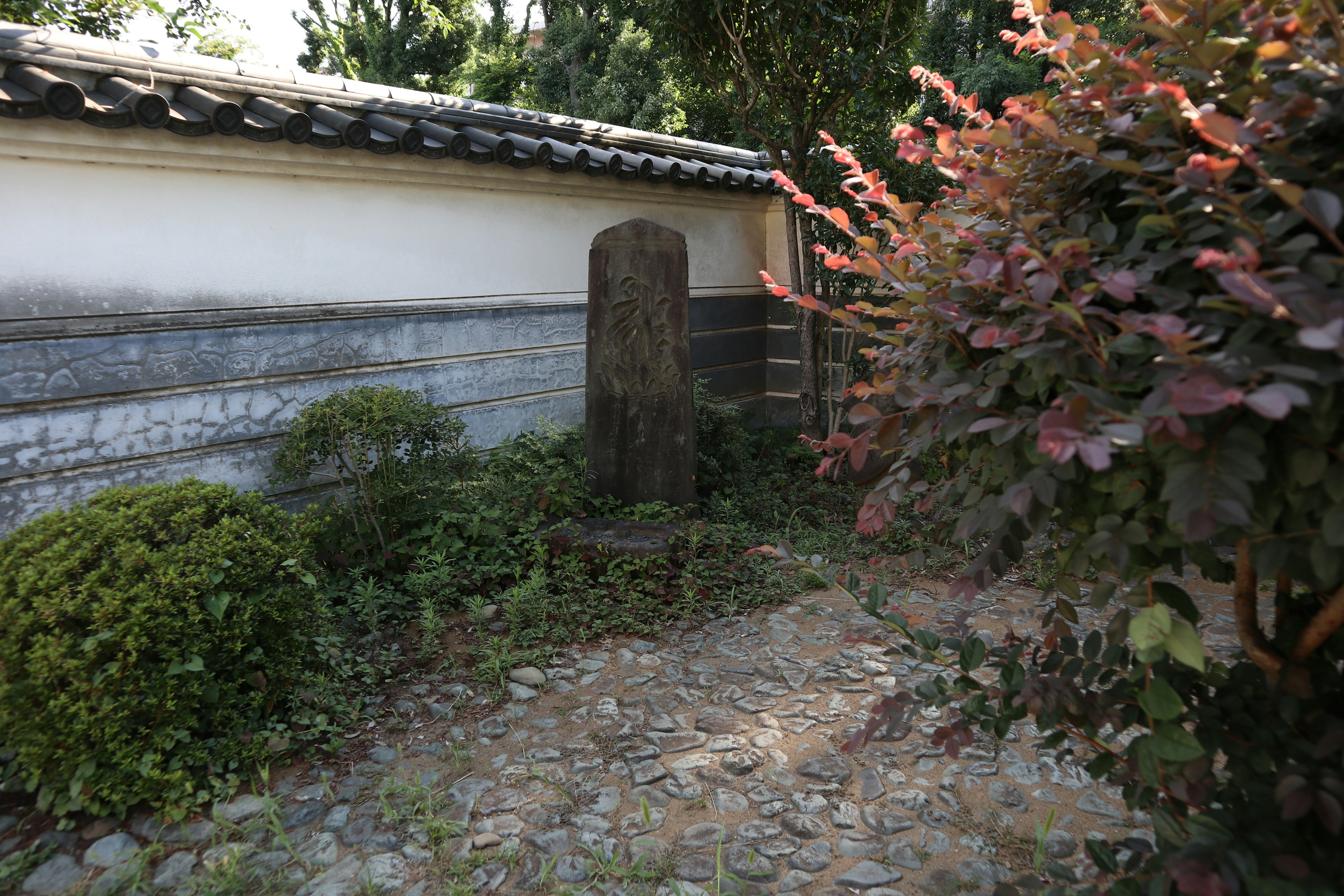 Sudut tenang taman Jepang dengan monumen batu dan vegetasi subur