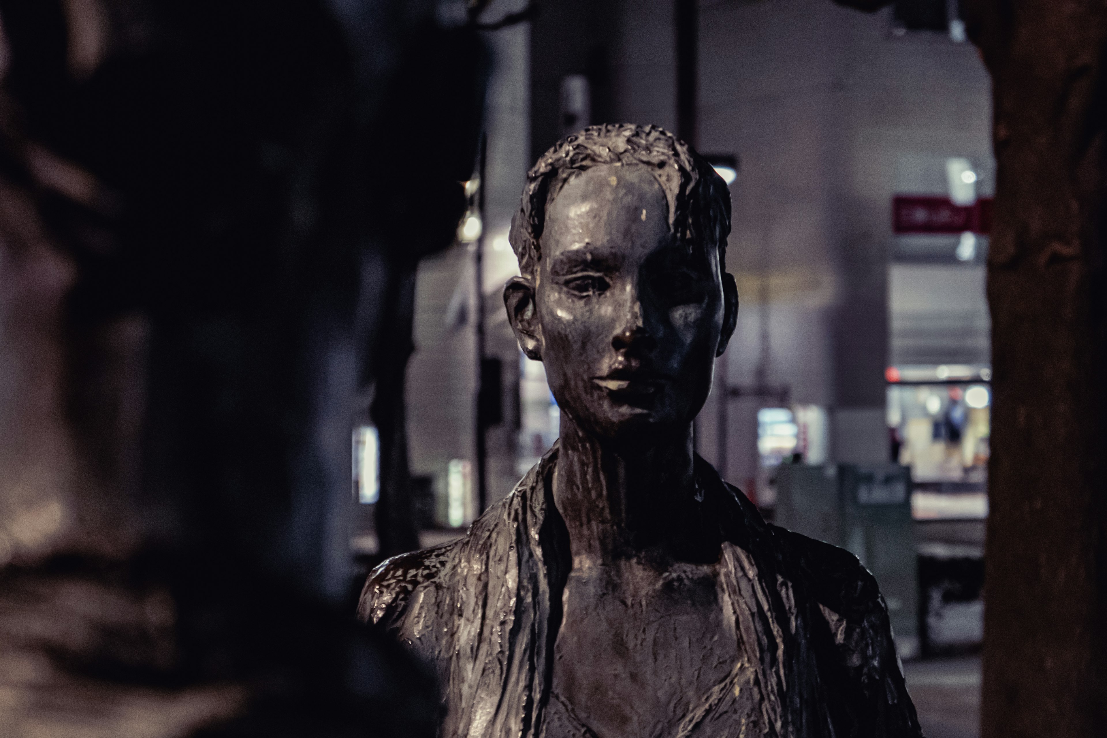 Metallic sculpture of a woman standing in a city at night gazing at another sculpture