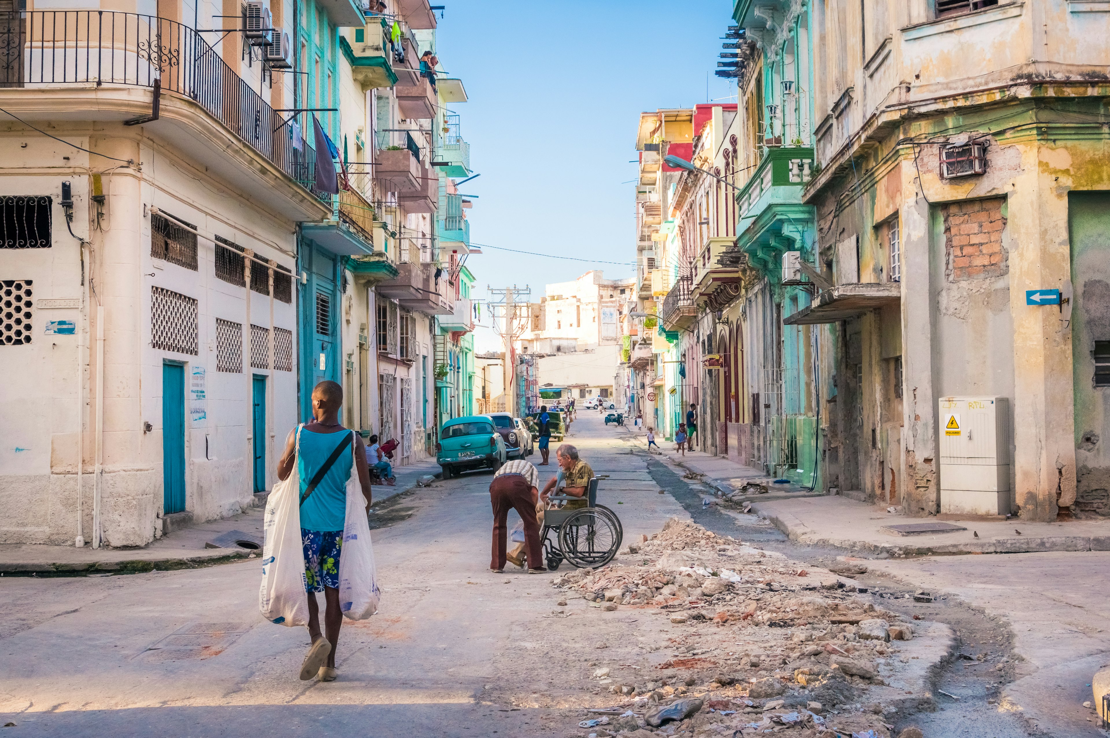 Edifici colorati lungo una strada dell'Avana con persone che camminano e lavorano a riparazioni