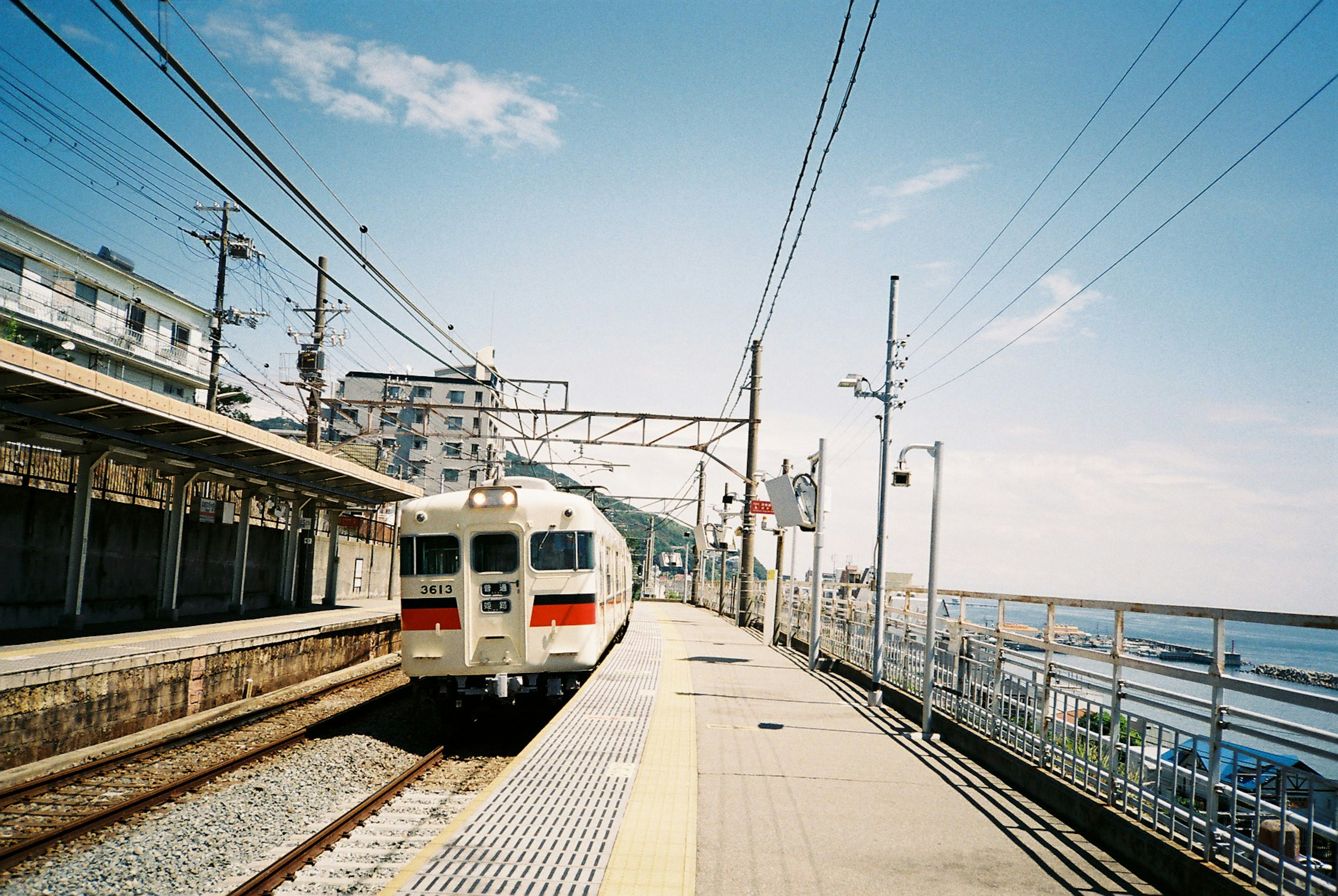 White train stopped at a station near the sea with a clear blue sky