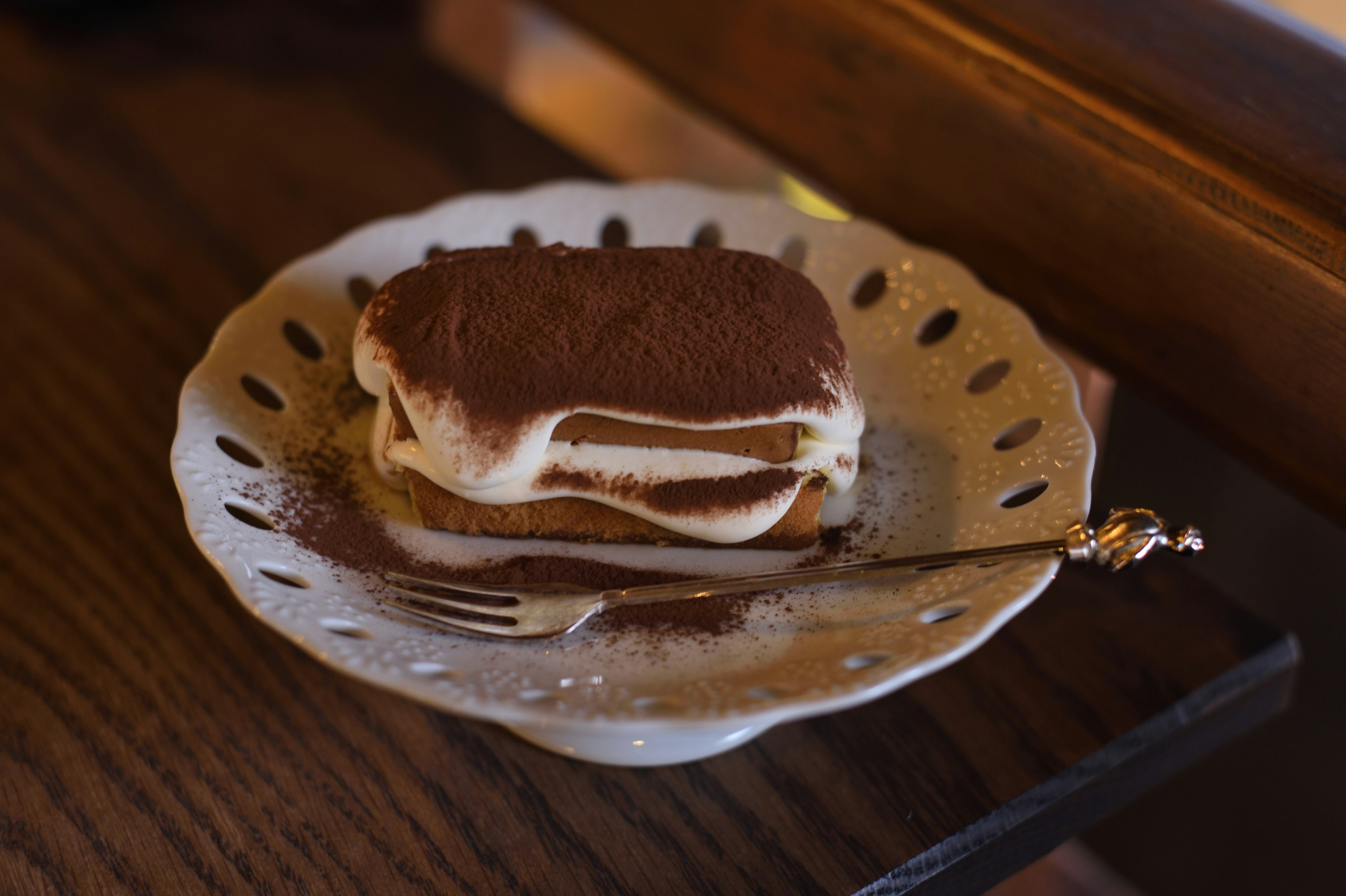 Tiramisu-Dessert auf einem dekorativen weißen Teller mit einer Gabel daneben