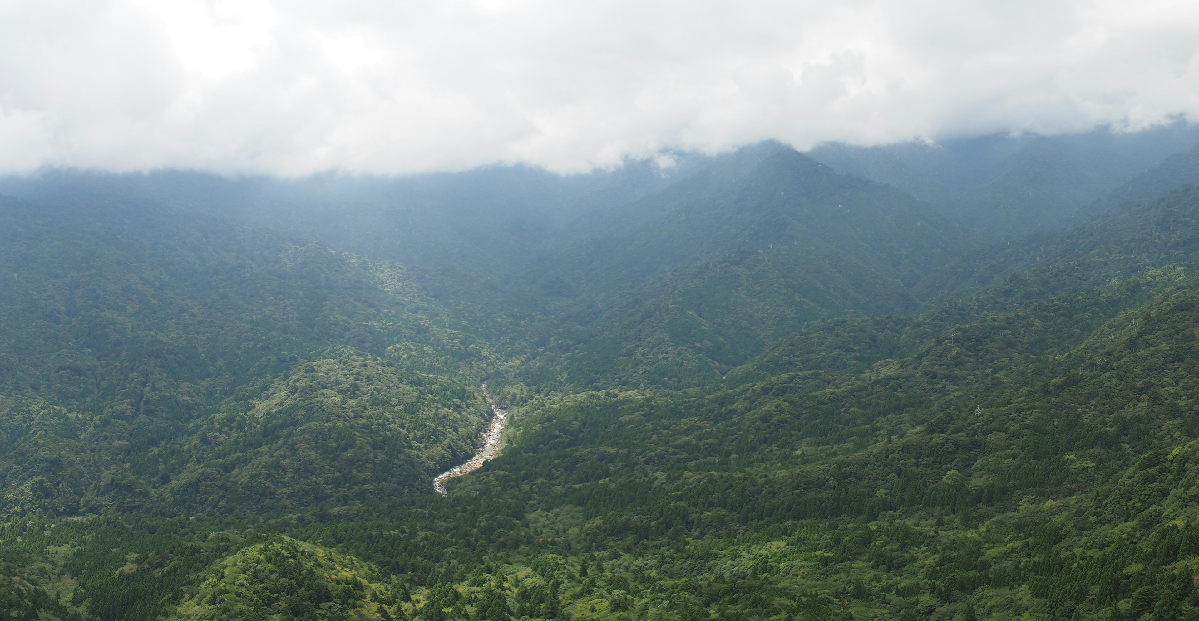 Pegunungan hijau subur dengan sungai berkelok di bawah langit mendung