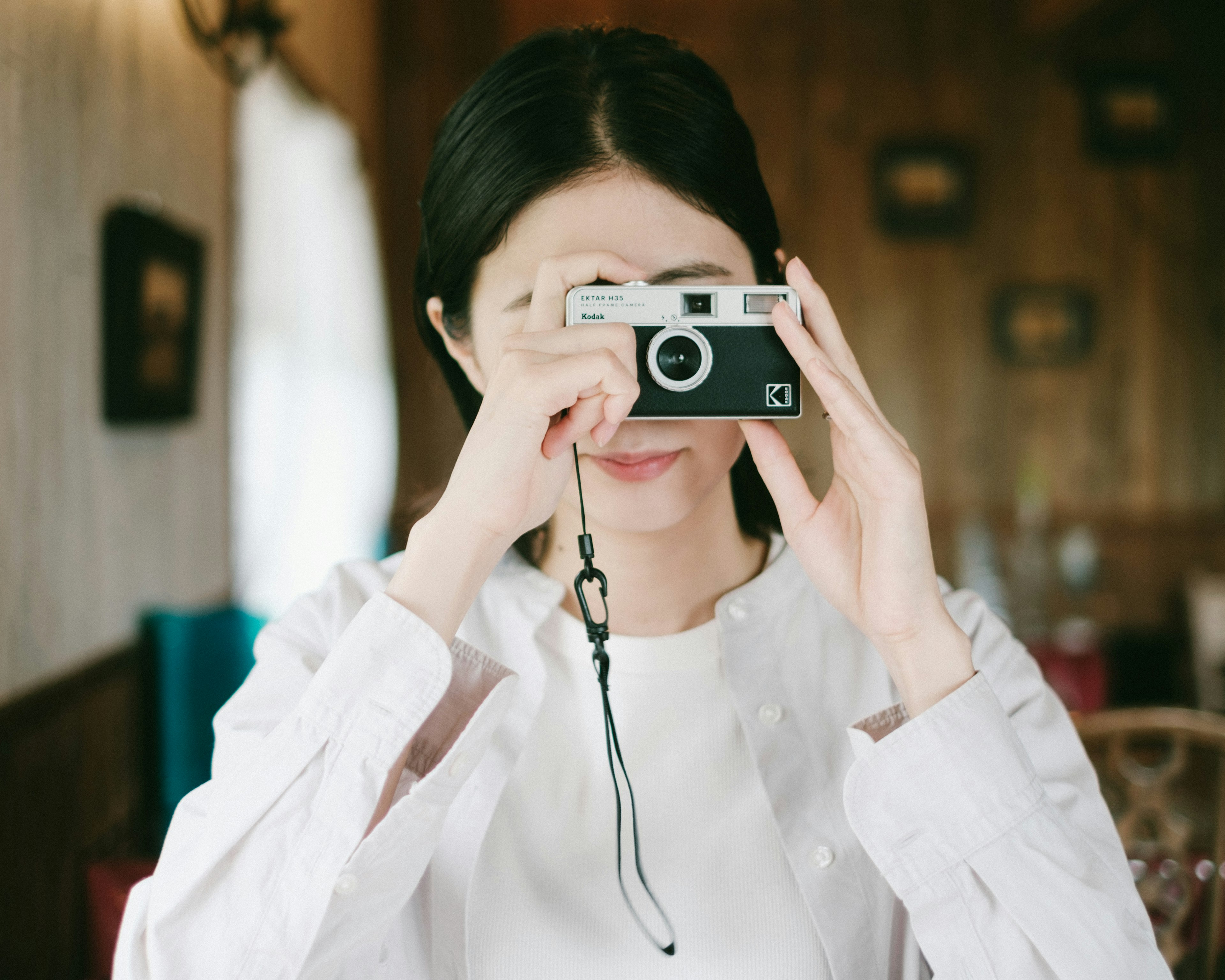 흰 셔츠를 입은 여성이 나무 인테리어에서 카메라를 들고 있다