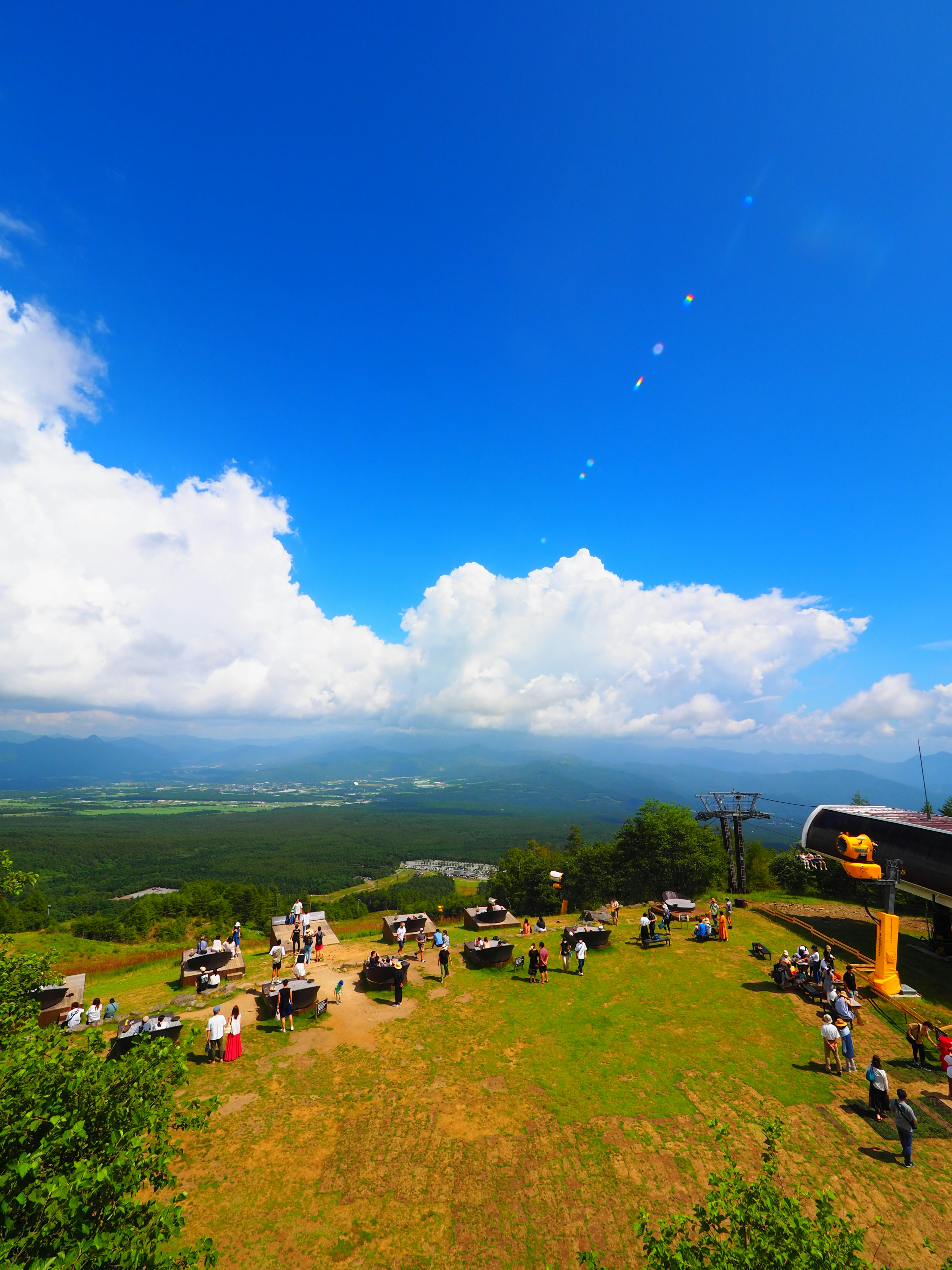 青空と白い雲が広がる山の頂上での風景 多くの人々がリラックスしている様子