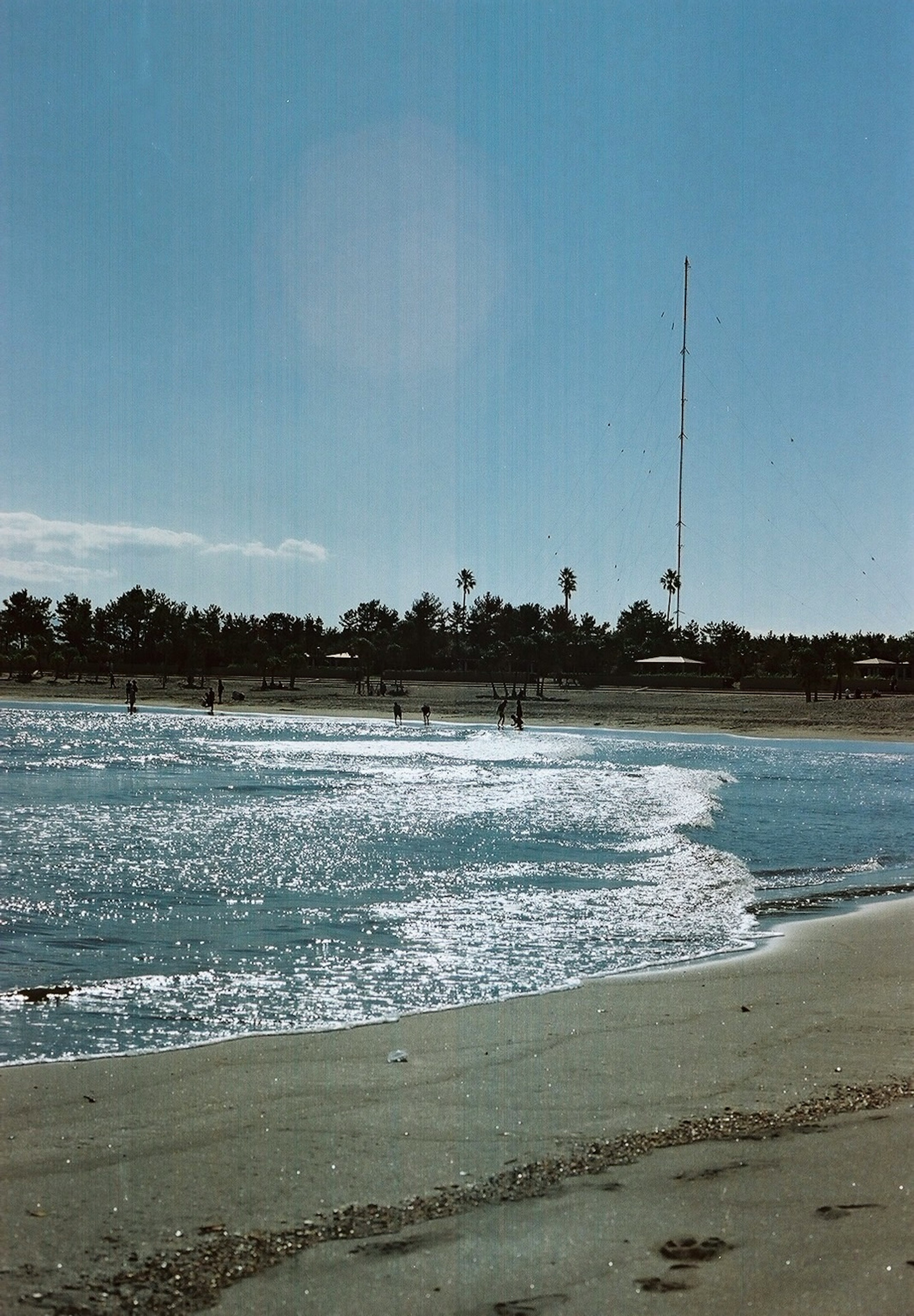 Pemandangan pantai dengan ombak dan langit biru menampilkan antena tinggi