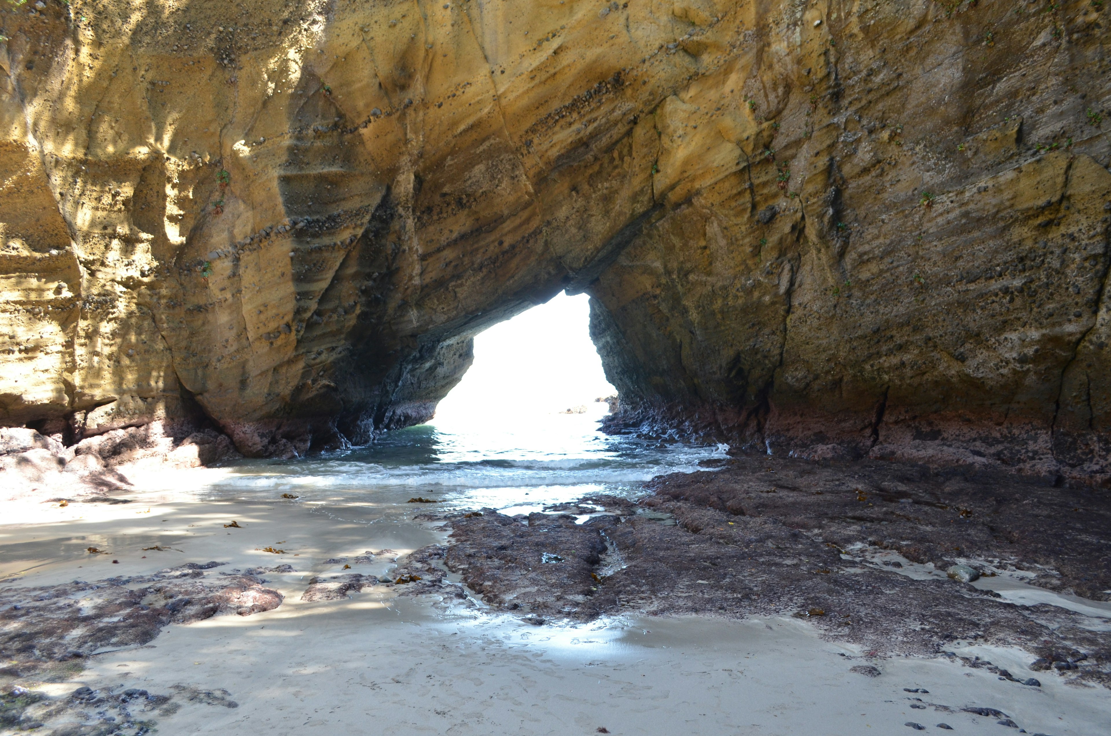 View through a rock archway to the bright ocean beyond and sandy beach