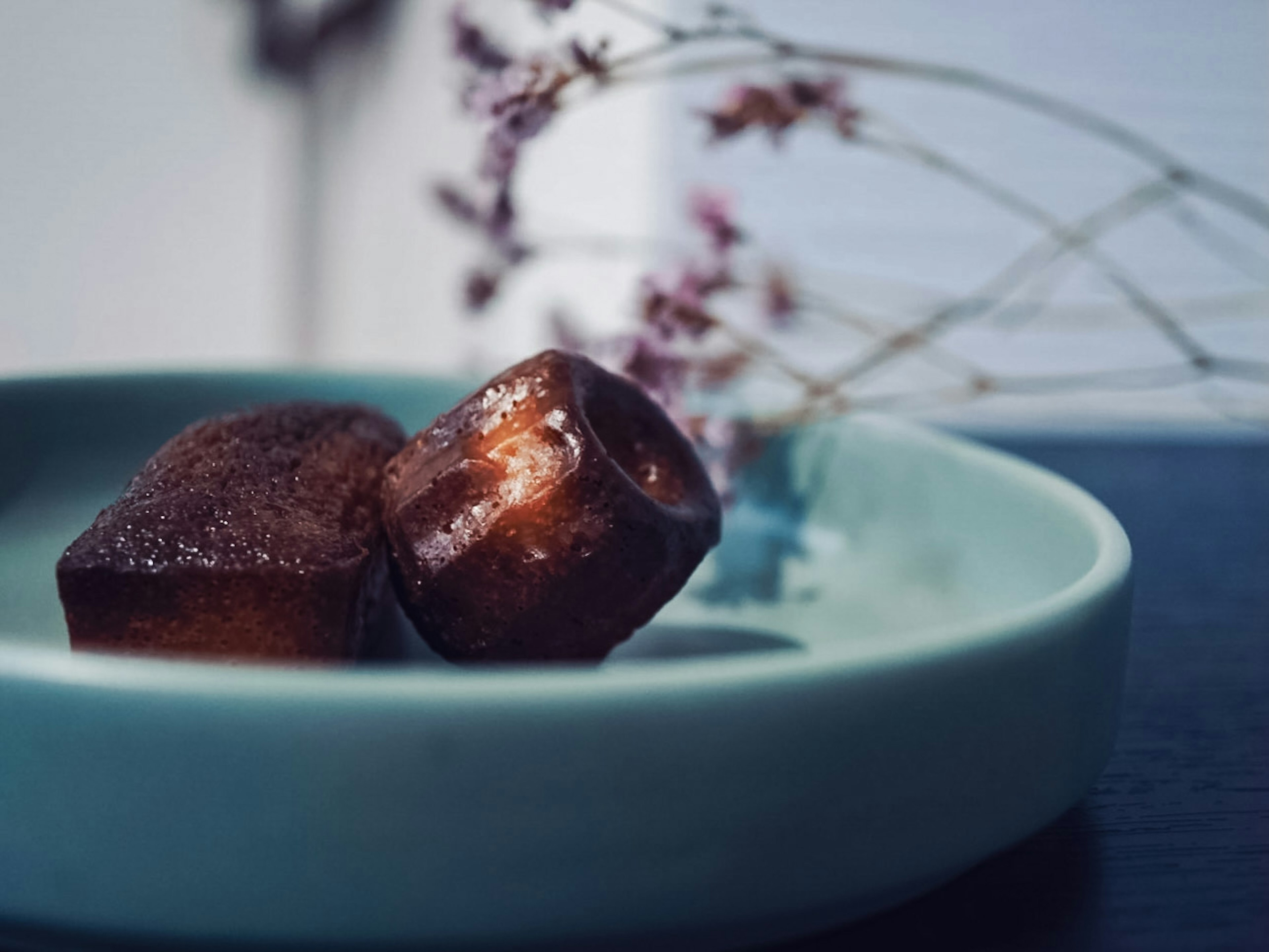 Two brown confections on a blue plate with flowers in the background