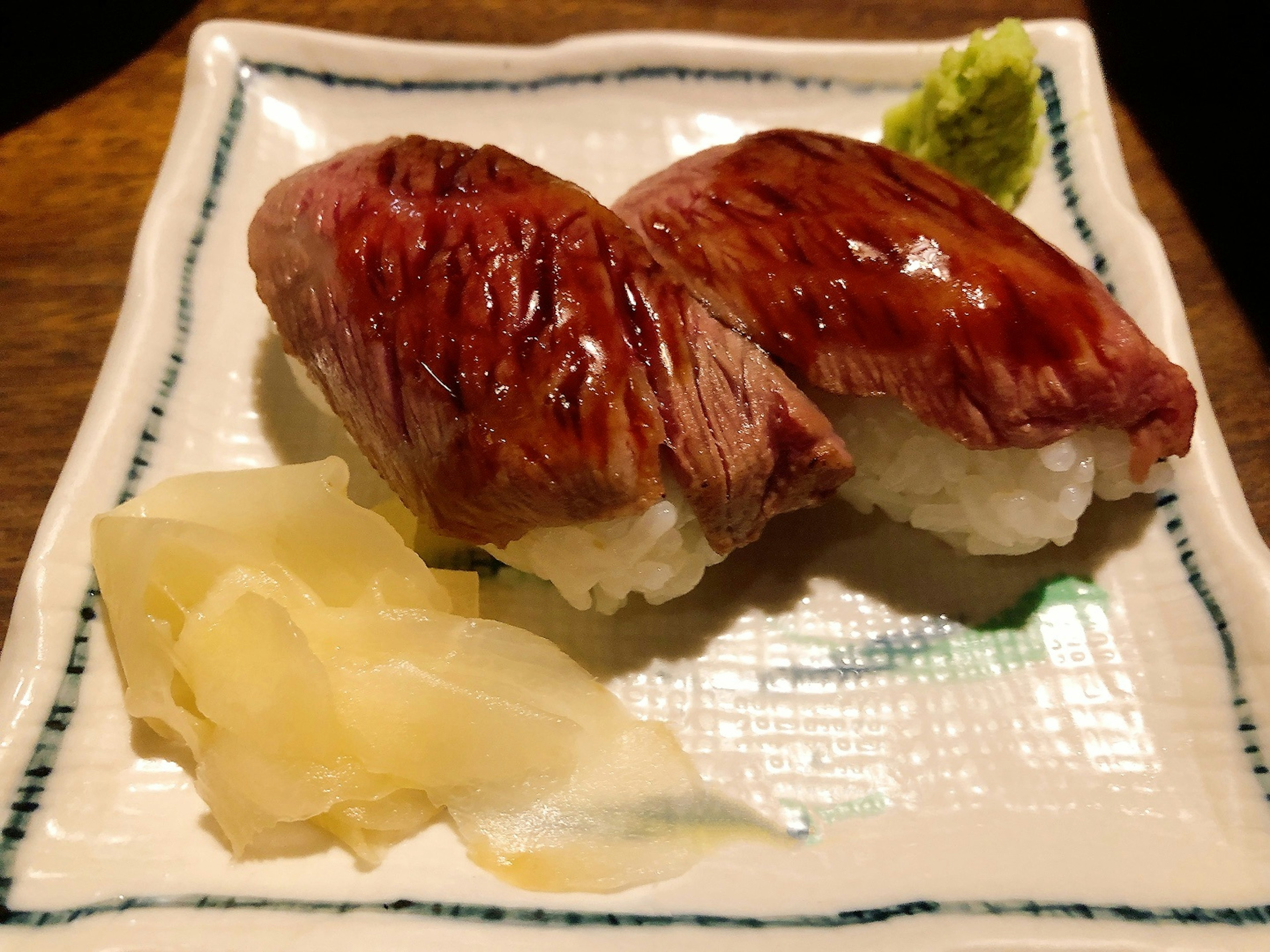 Two pieces of sushi on a plate with wasabi and pickled ginger