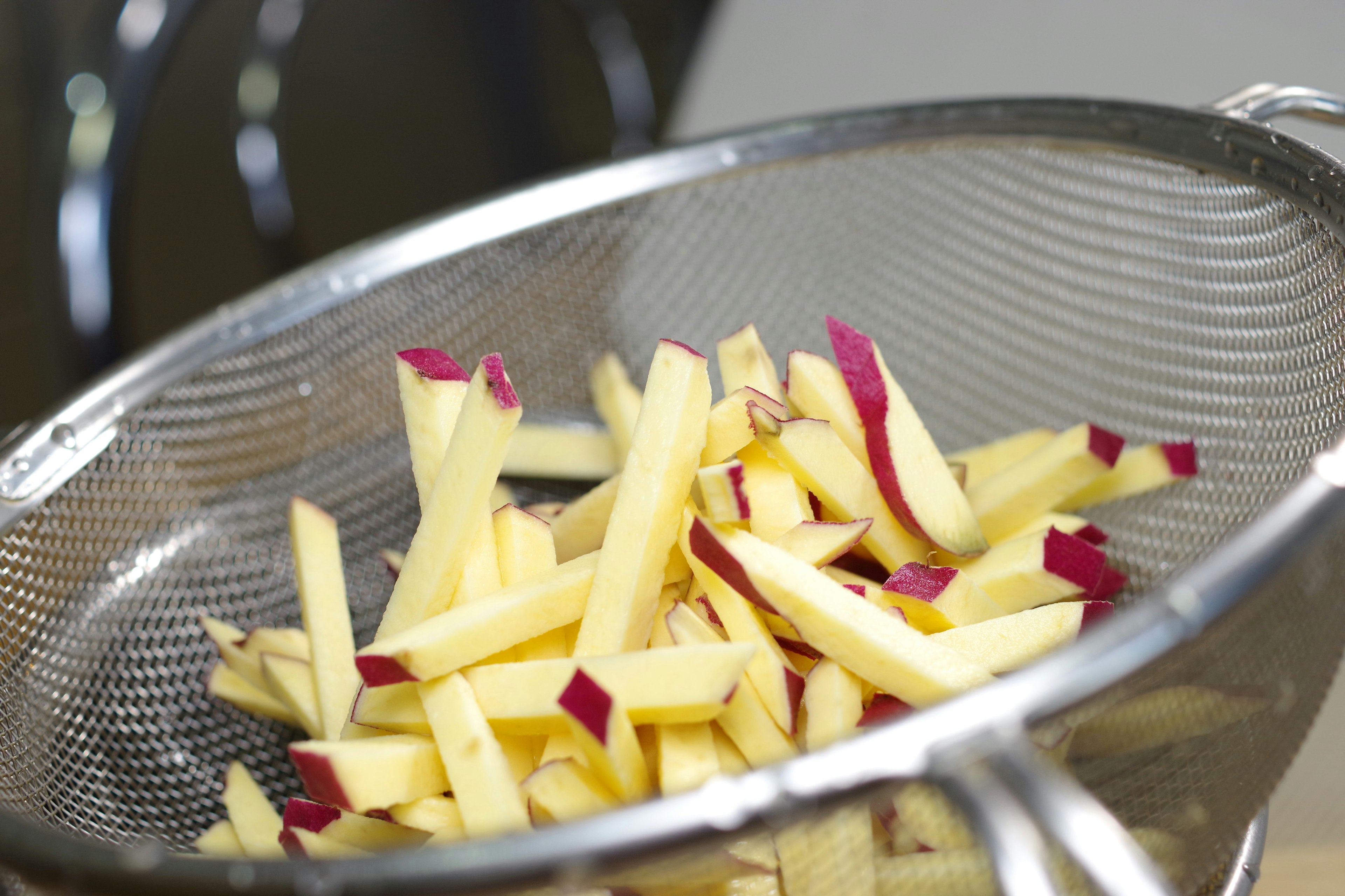 Long strips of sweet potato in a colander for draining