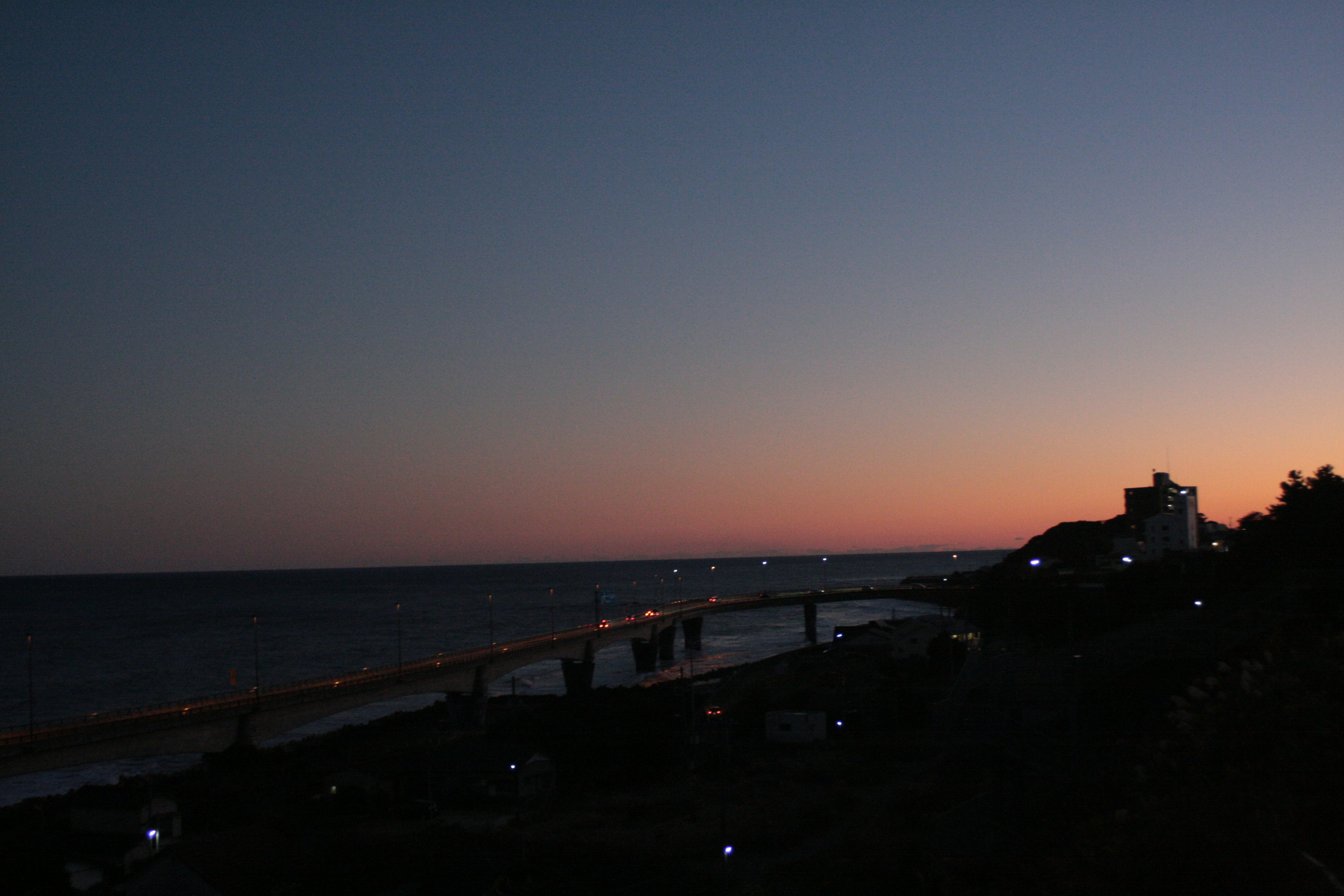 Vista costera al atardecer con un océano sereno y luces distantes