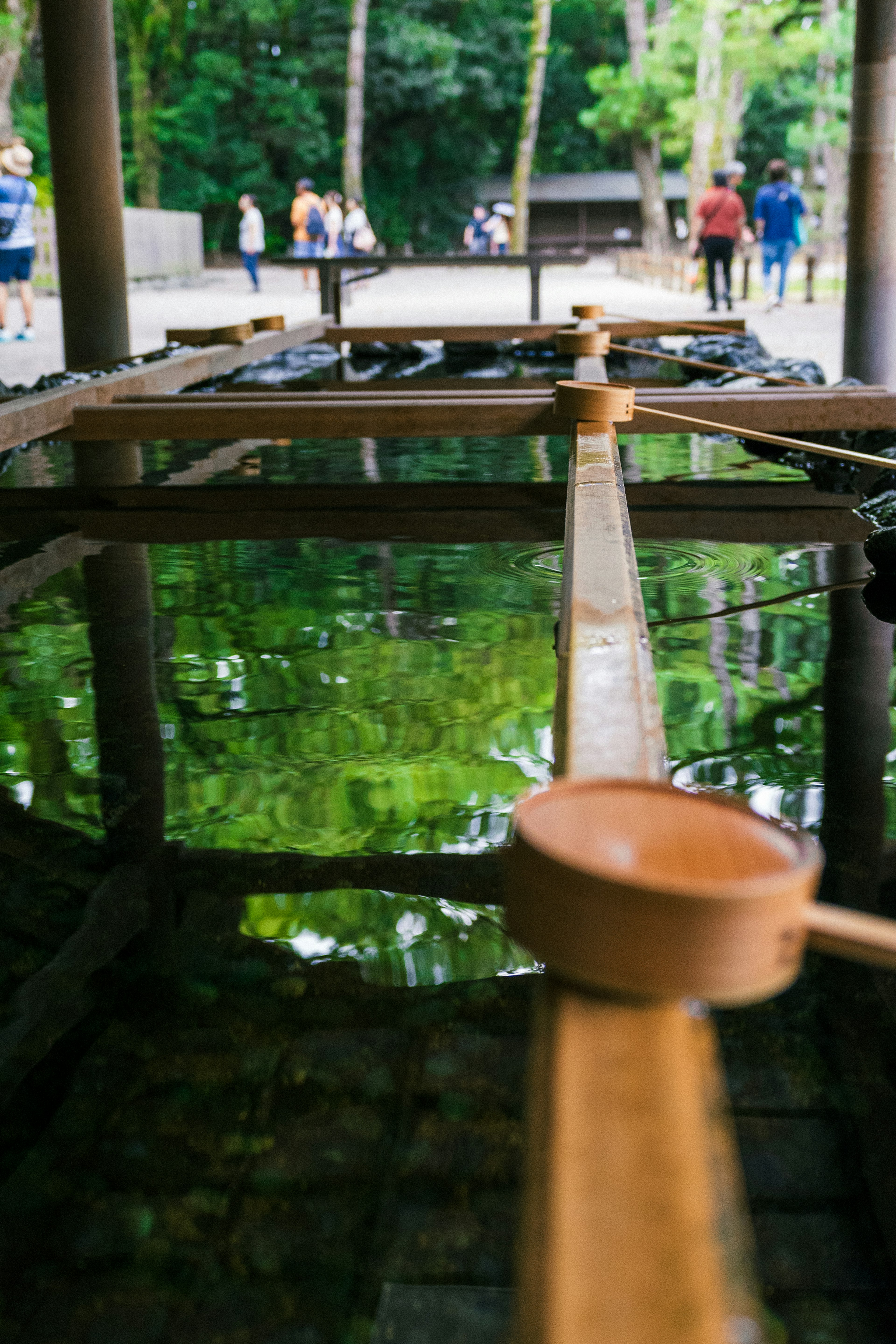 Wooden water basin reflecting green water with a ladle in the foreground