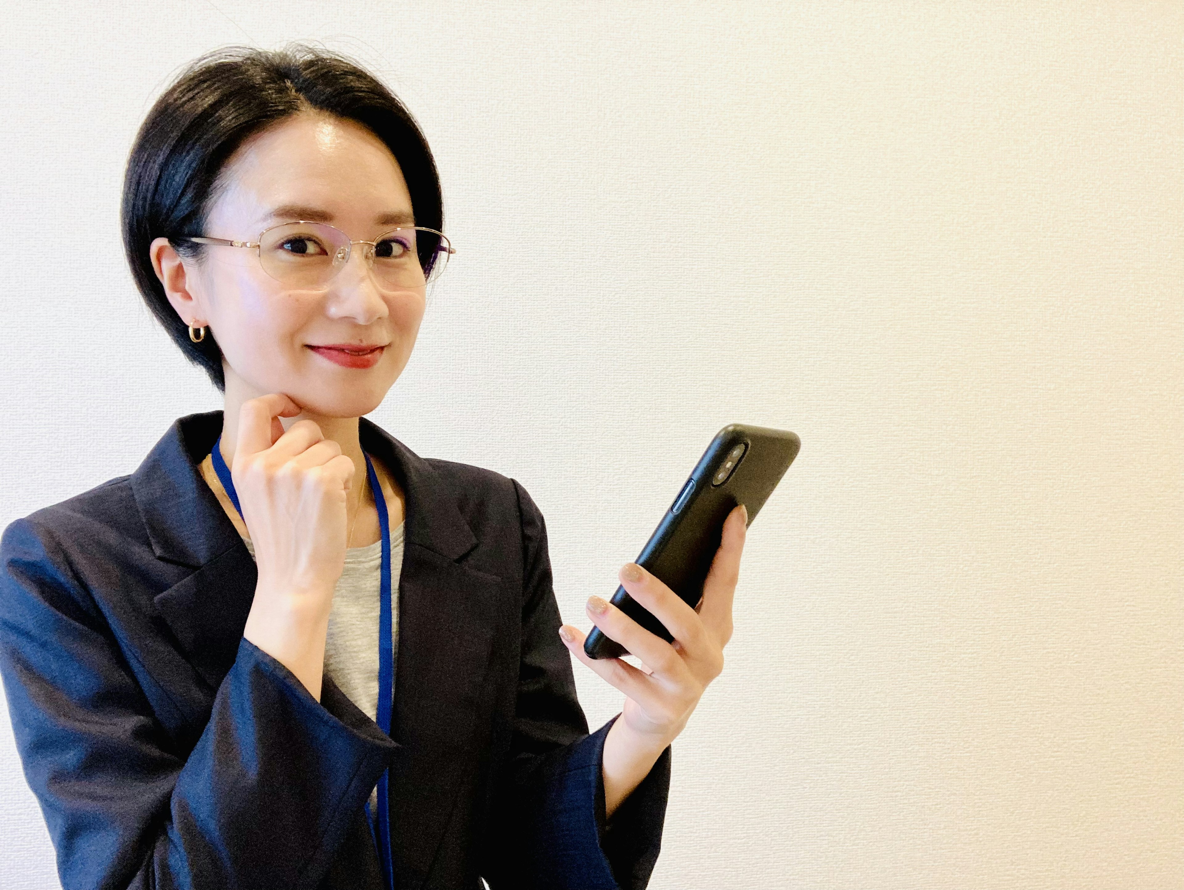 黒いスーツを着た女性がスマートフォンを持って微笑んでいる