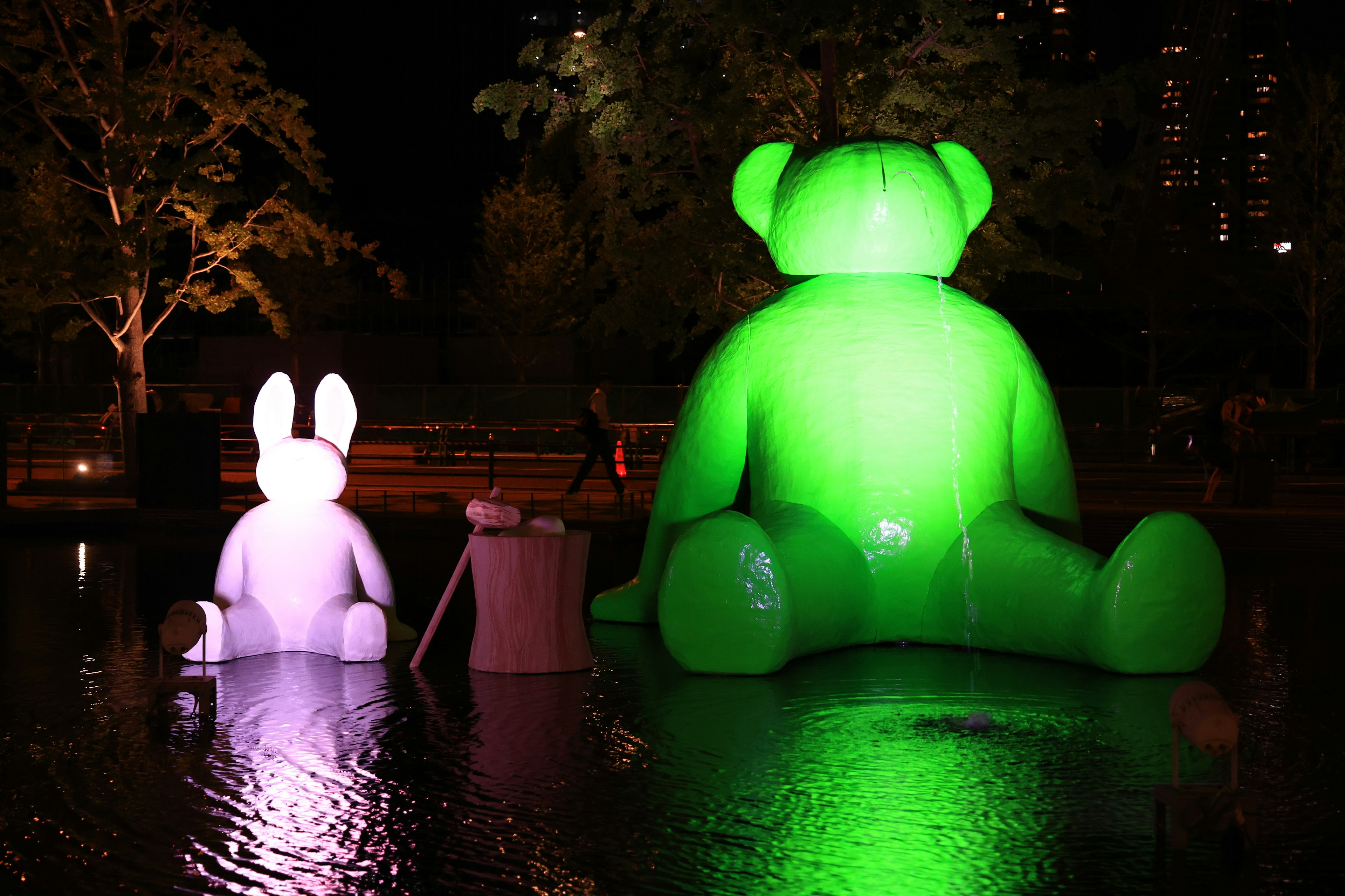 夜の池で輝く緑のクマと白いウサギの大きなオブジェ