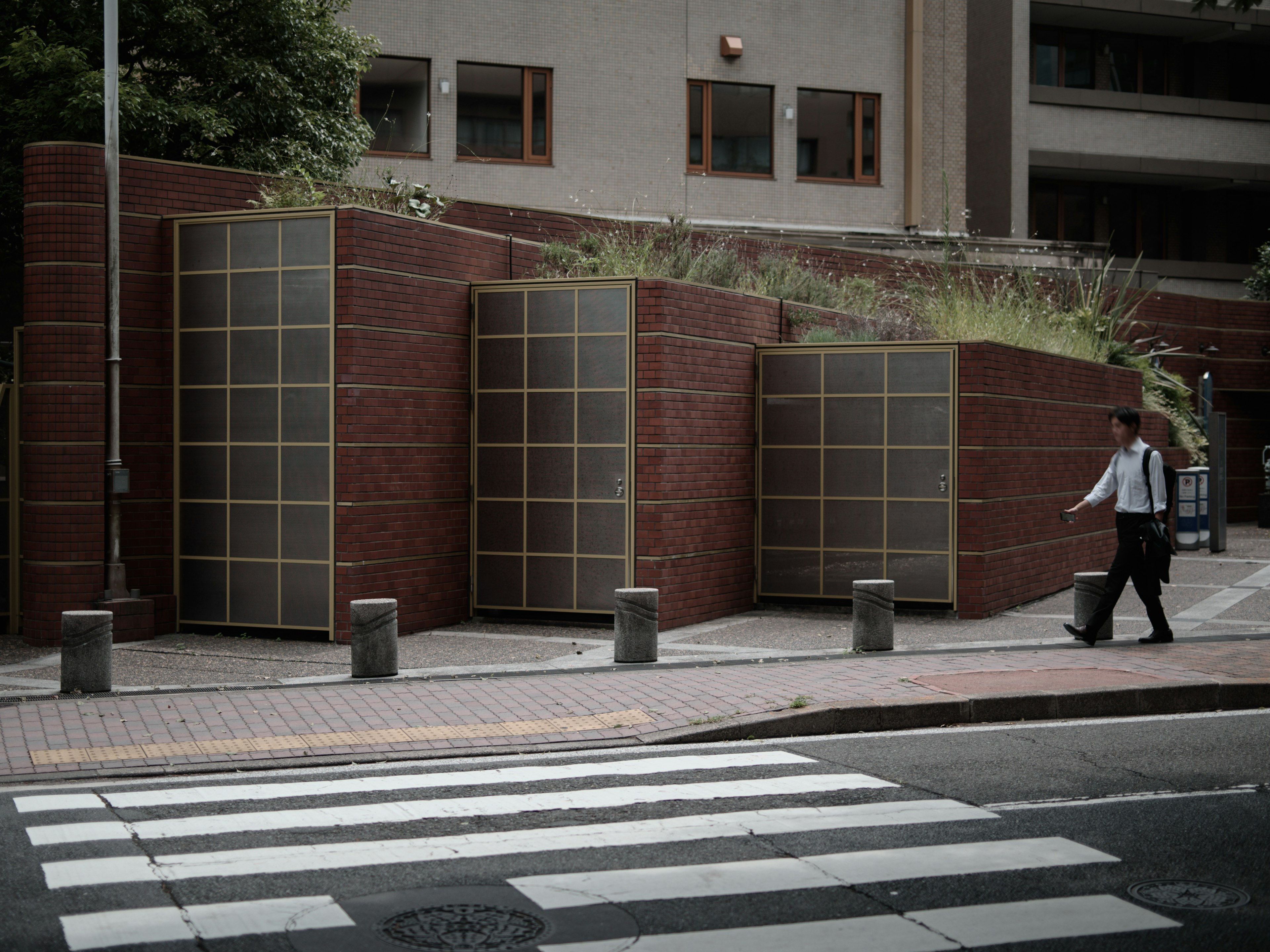 ビジネスマンが横断歩道を歩いている背景にある現代的な建物とレンガの壁